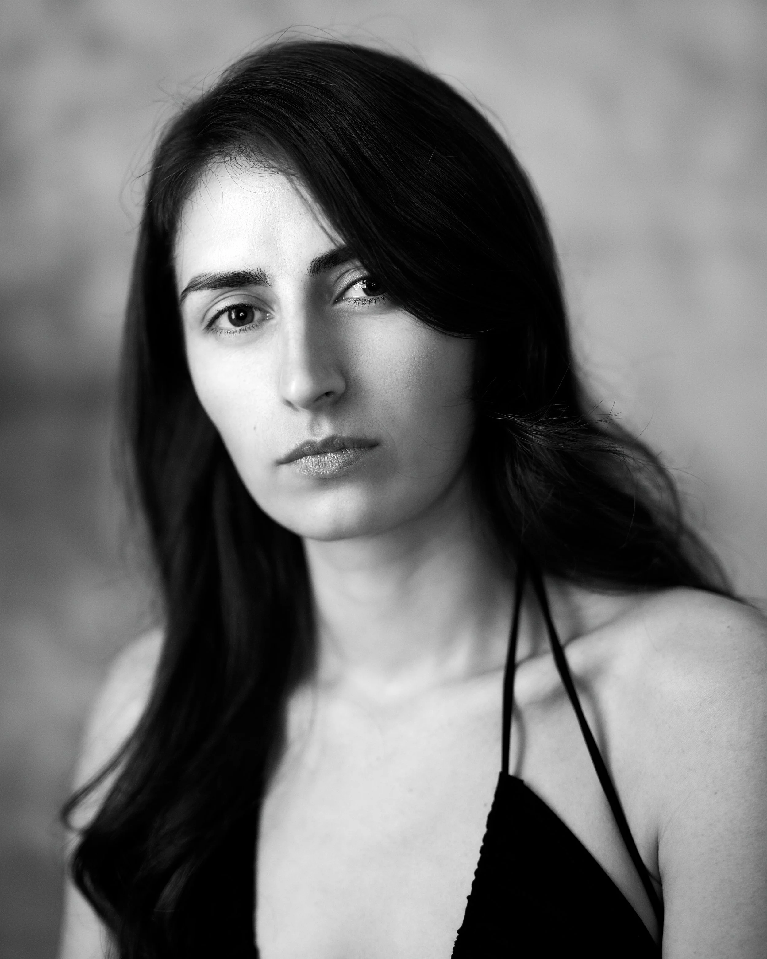 Black and white portrait of a young woman with dark hair, looking directly at the camera with a neutral expression.