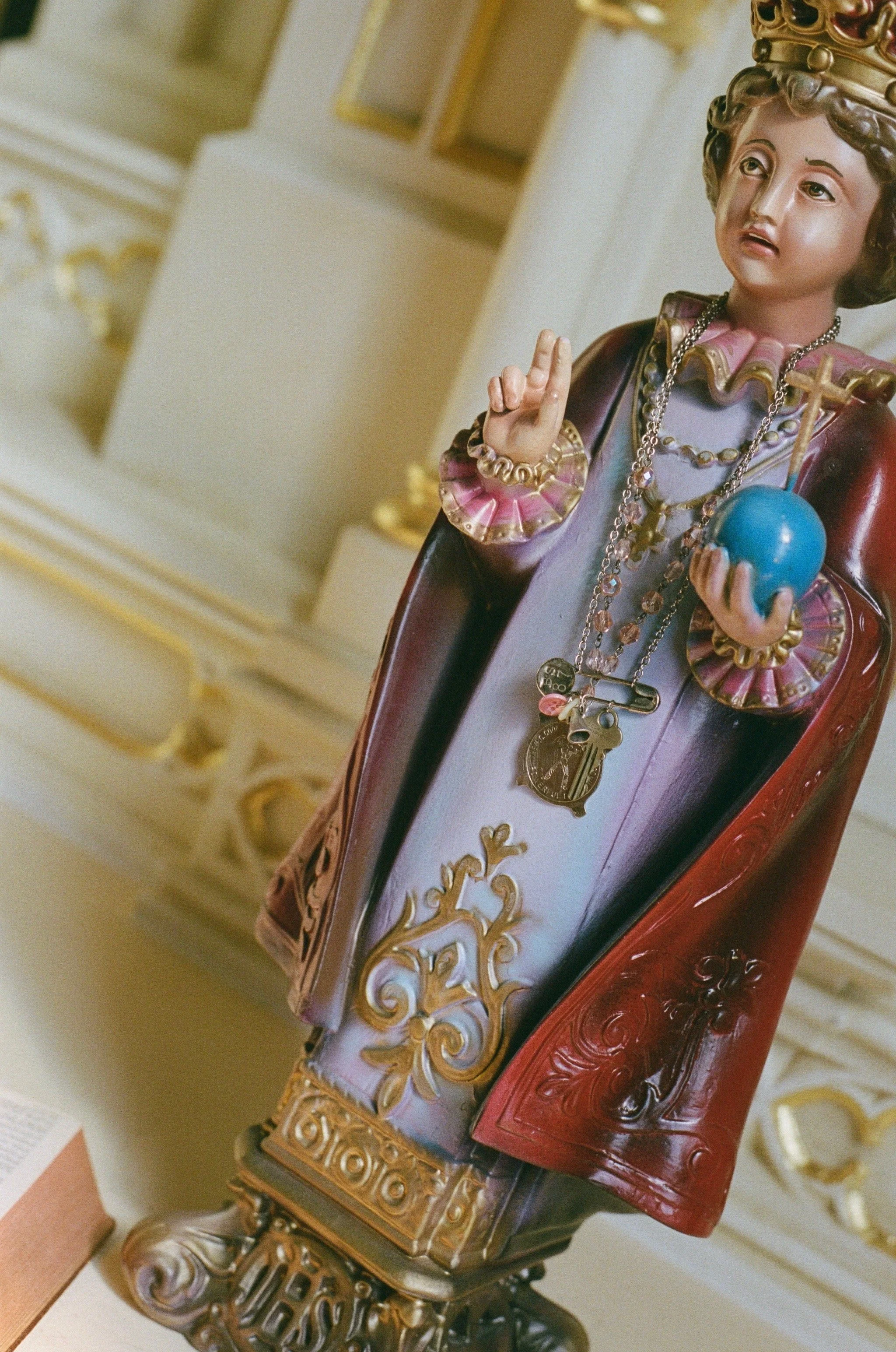 A religious statue holding a blue orb and making a gesture with the right hand, dressed in colorful robes with gold accents, in an ornate setting.