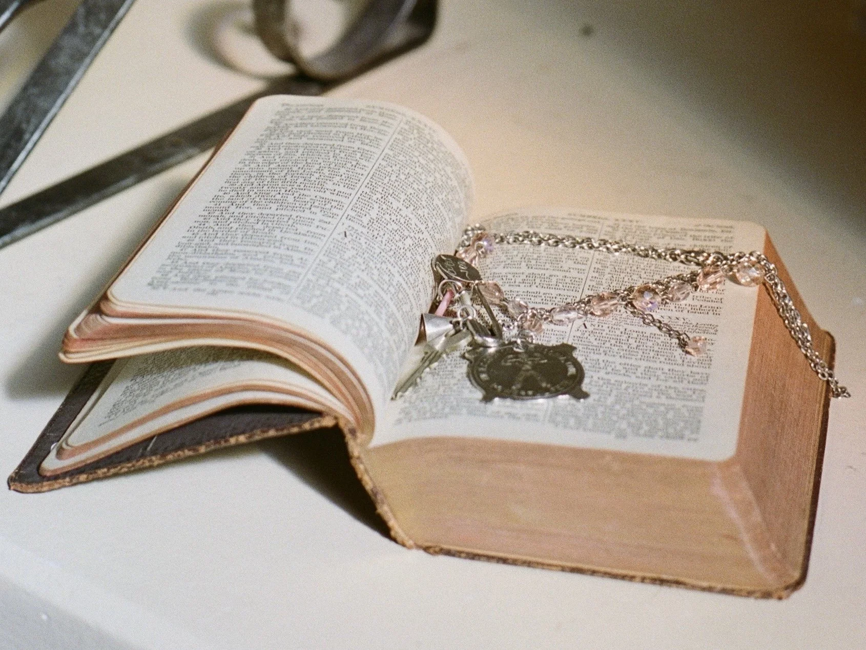 An open, well-worn book with a silver chain and jewelry placed on its pages.
