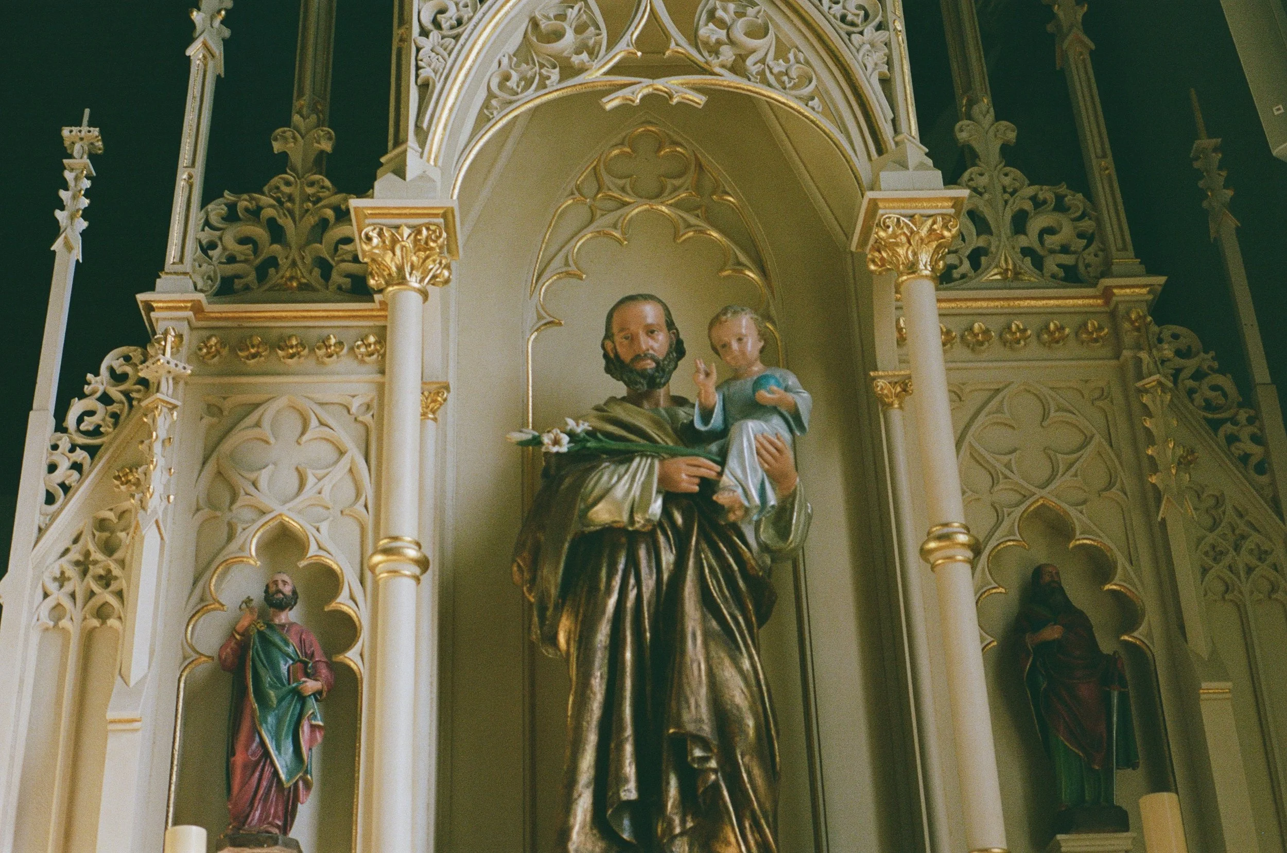 Religious statue of a man holding a child, placed in an ornate church altar with gold accents and decorative arches.