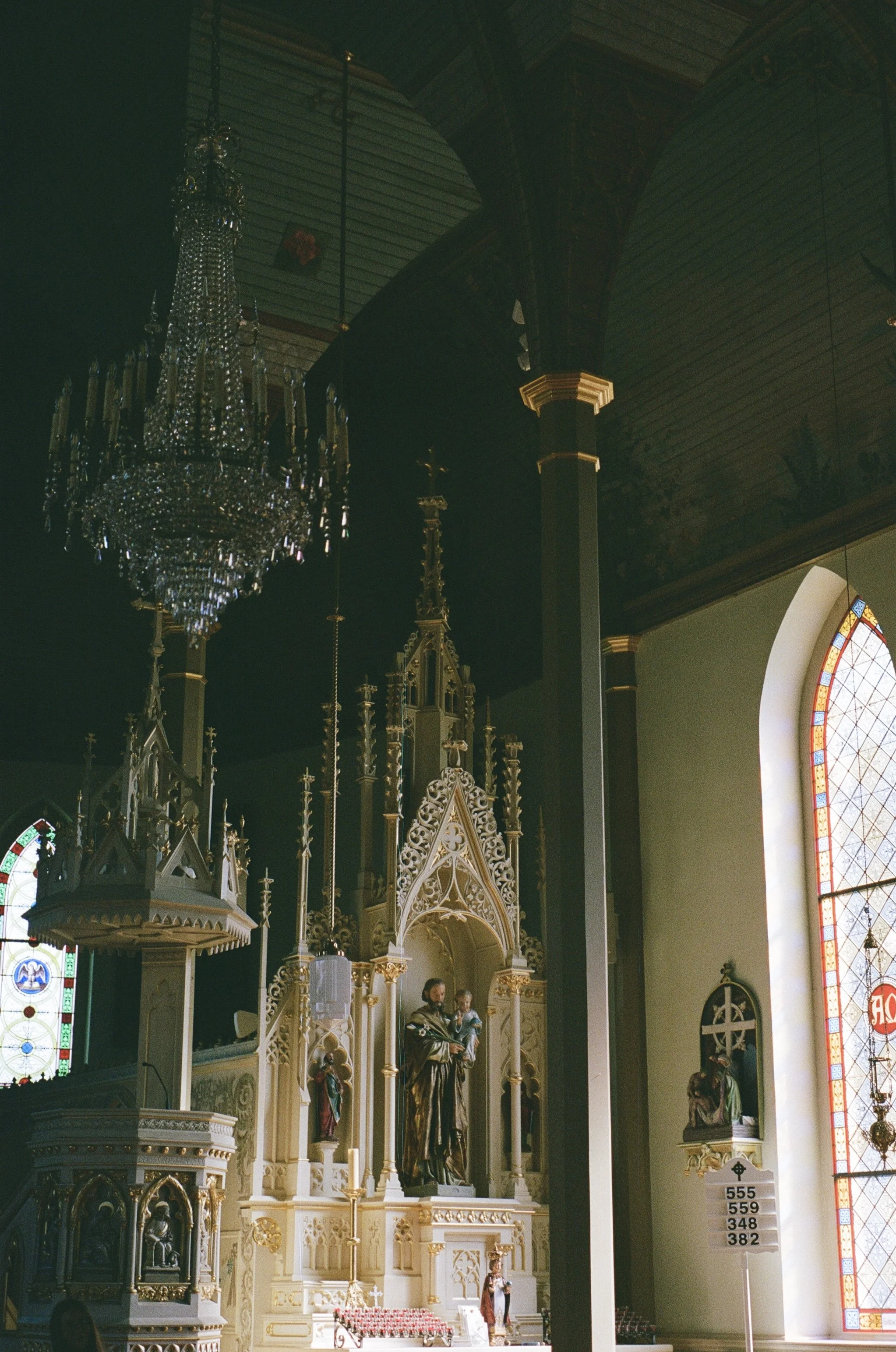 Interior of a church or cathedral with an ornate altar featuring religious statues, stained glass windows, a chandelier, and architectural details with gold accents.