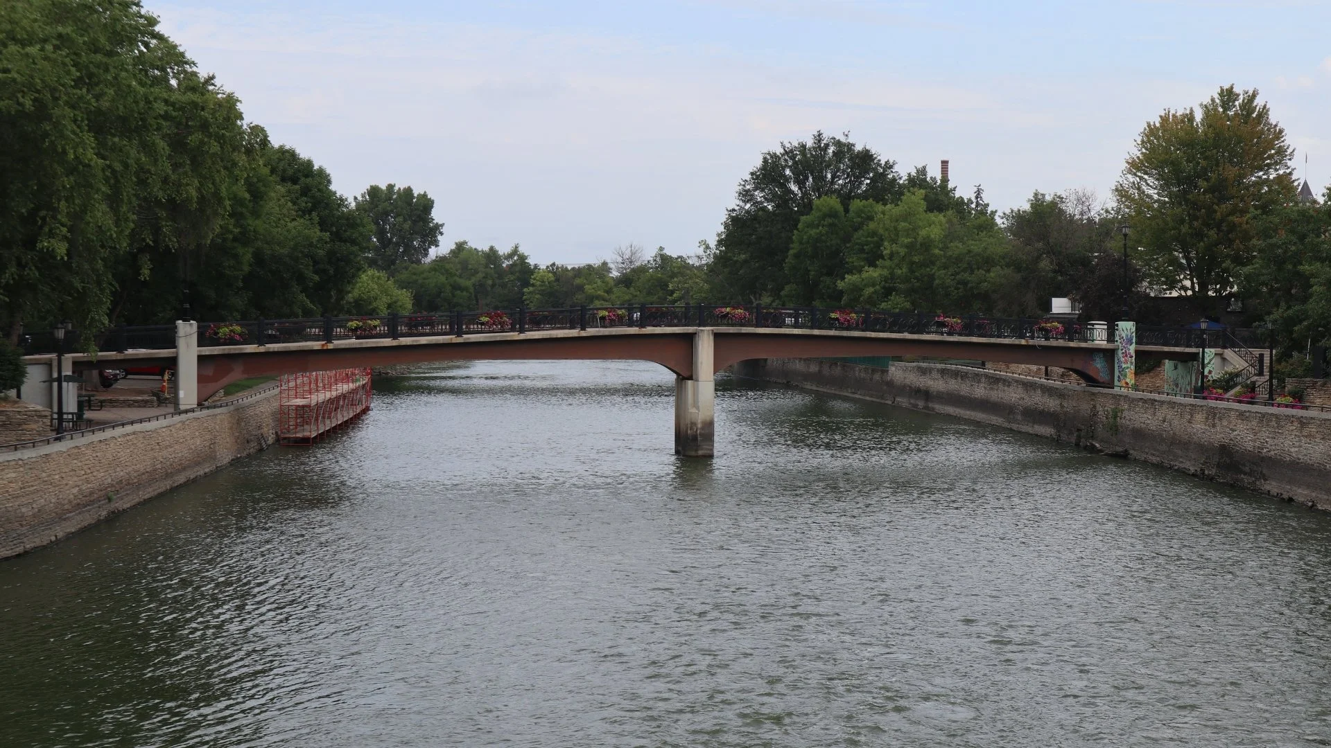 A river flowing underneat a foot bridge with greenery in the background.