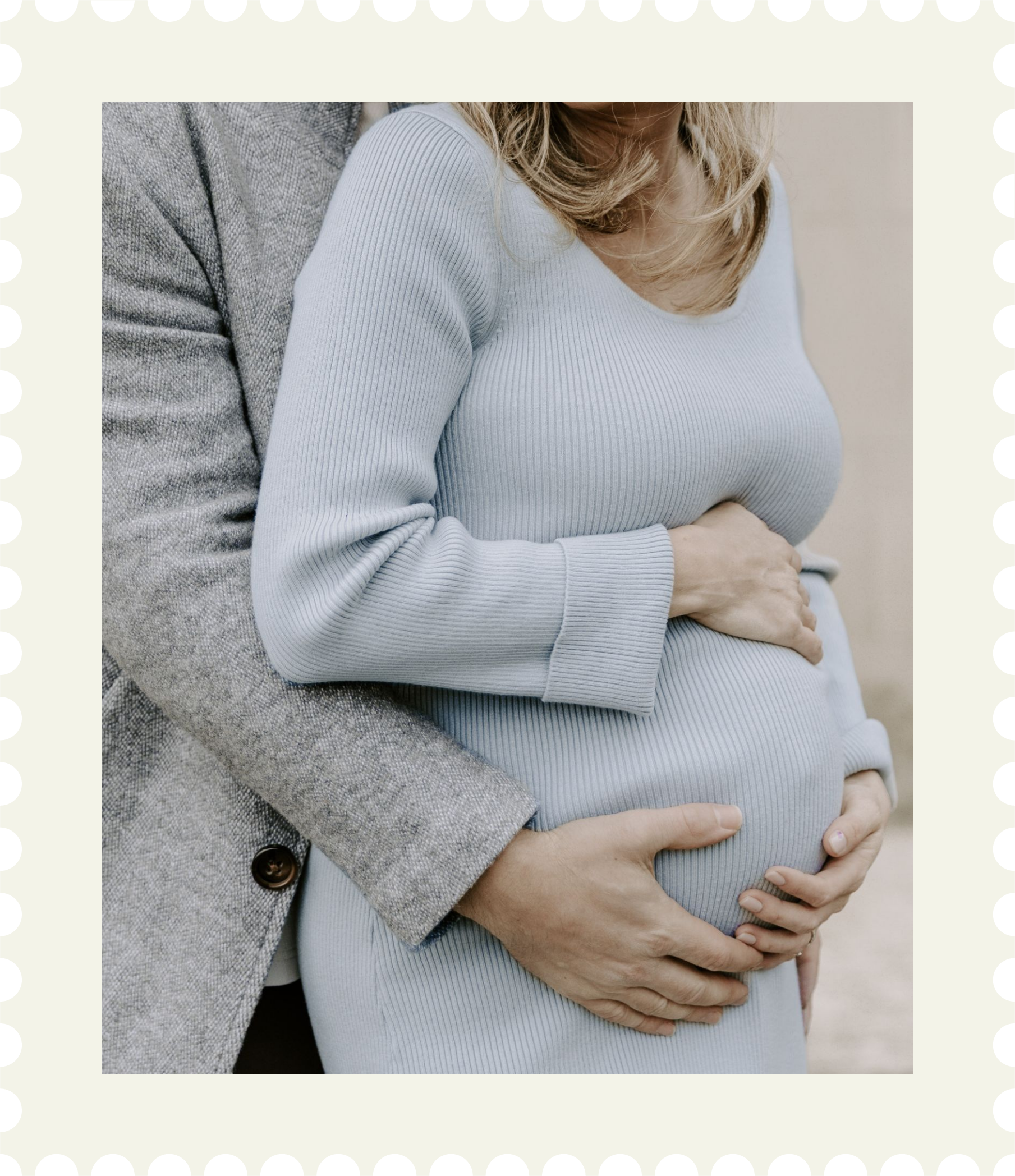 A pregnant woman in a light gray ribbed long-sleeve top being comforted and supported by a man in a gray plaid blazer, with her hands resting on her pregnant belly for maternity photography package in Brockville Ontario.