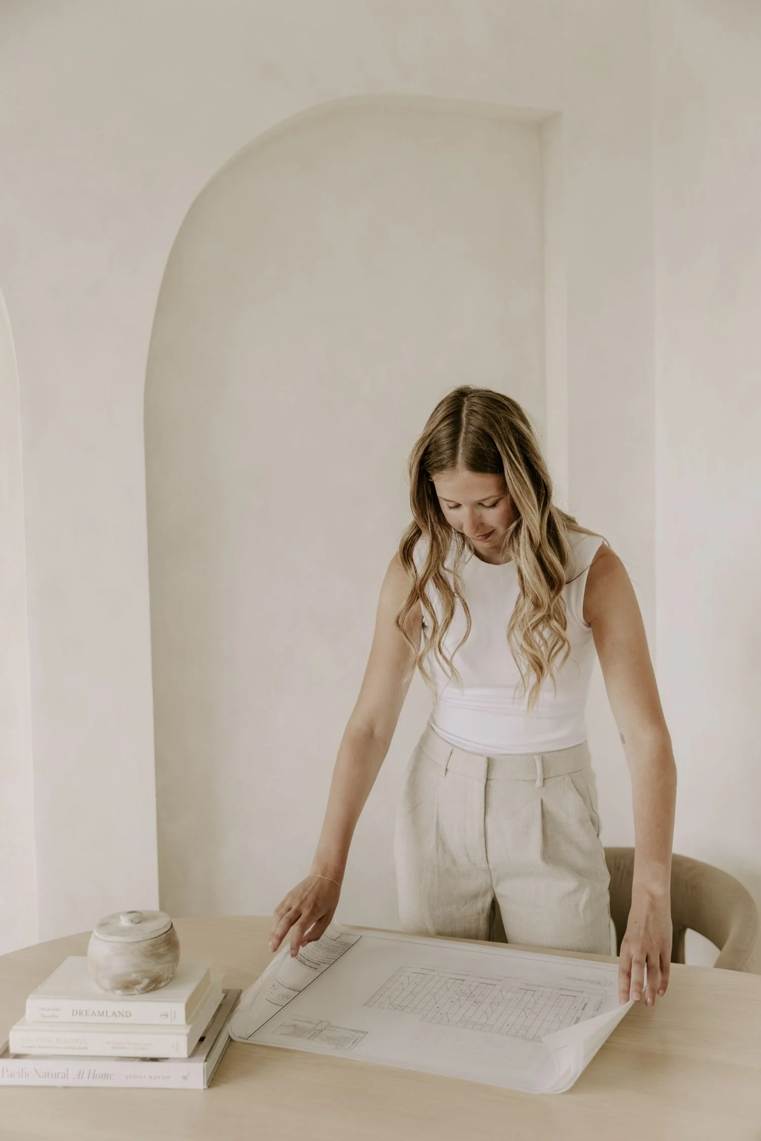 Woman leaning over a table with architectural blueprints and books, including a white ceramic vase and a closed notebook for branding photography package in Ontario.