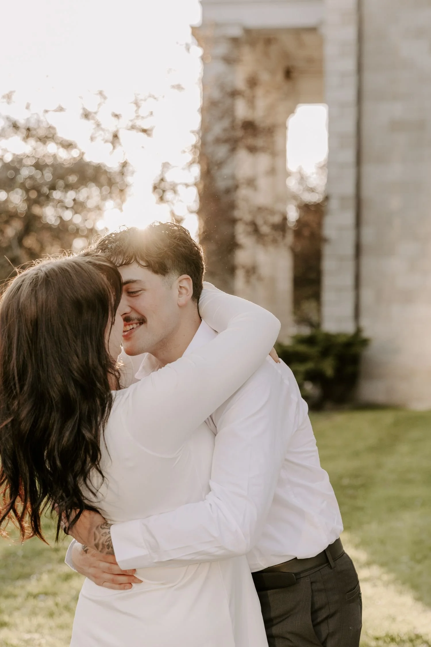 A couple embracing outdoors, with the sun setting behind them near a large stone monument for couples photography package in Eastern Ontario.