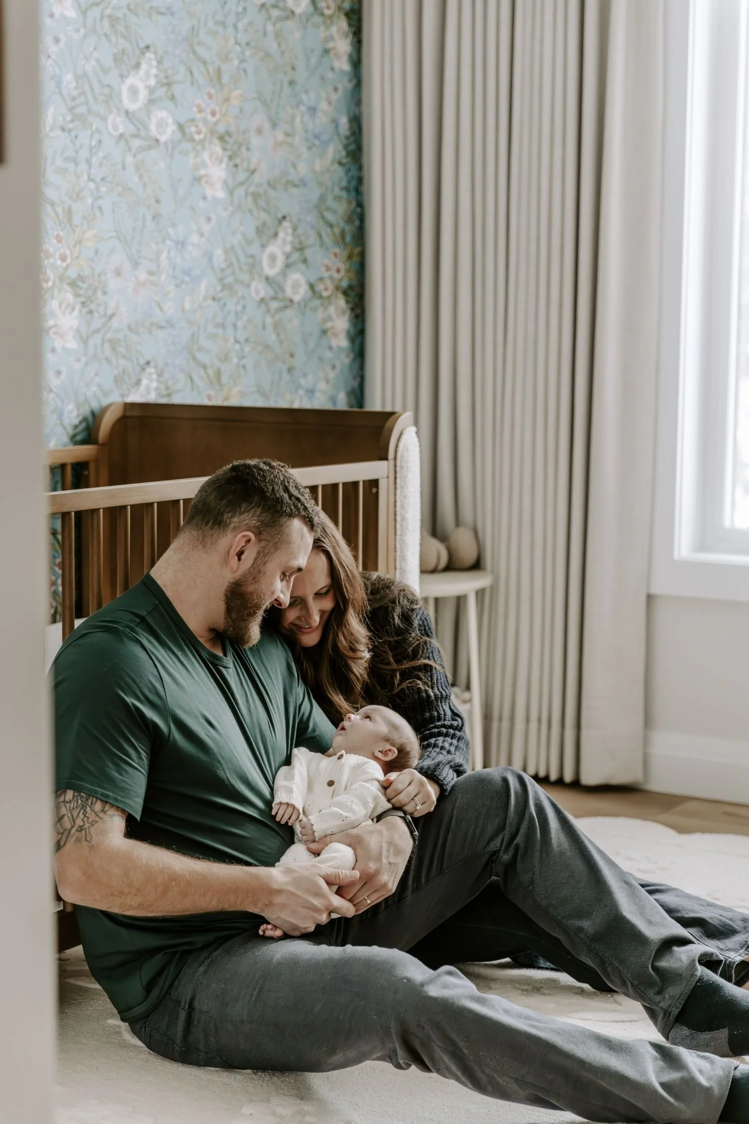 A family sitting on the floor in a cozy, well-lit living room, with a man, woman, and baby for their newborn family photography session in Ottawa Ontario.