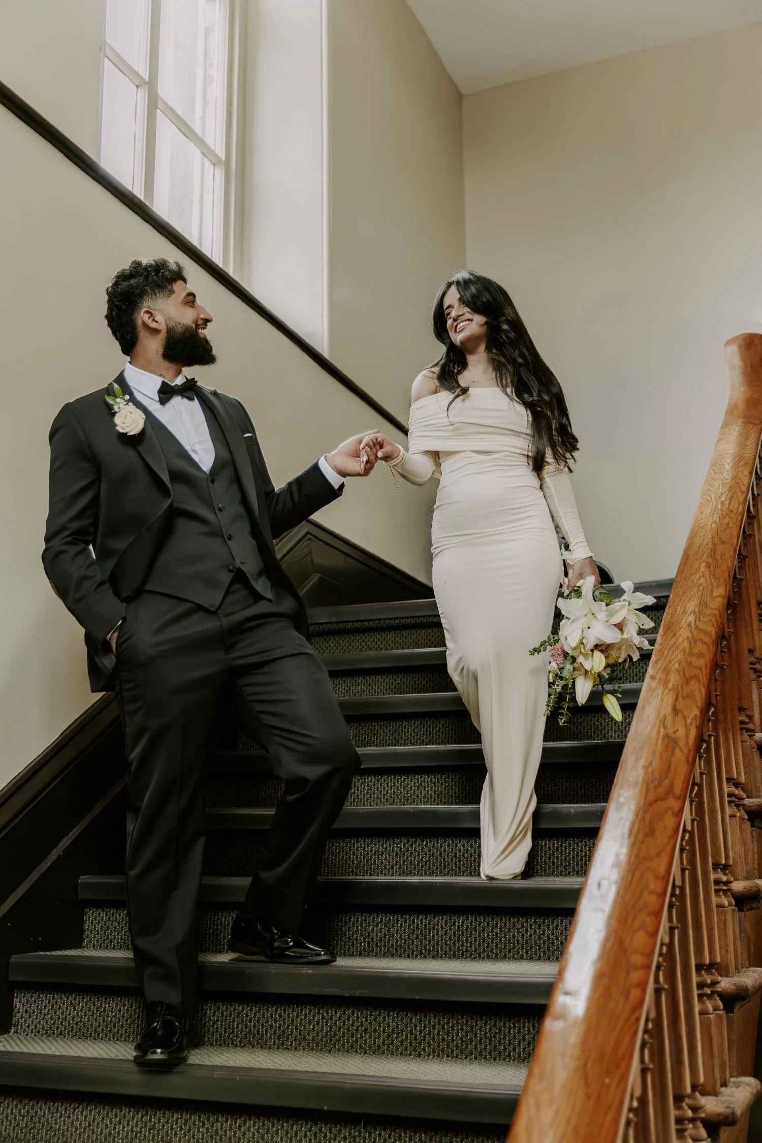 A couple, dressed in wedding attire, standing on a staircase and smiling at each other during their wedding photography package session in ontario.