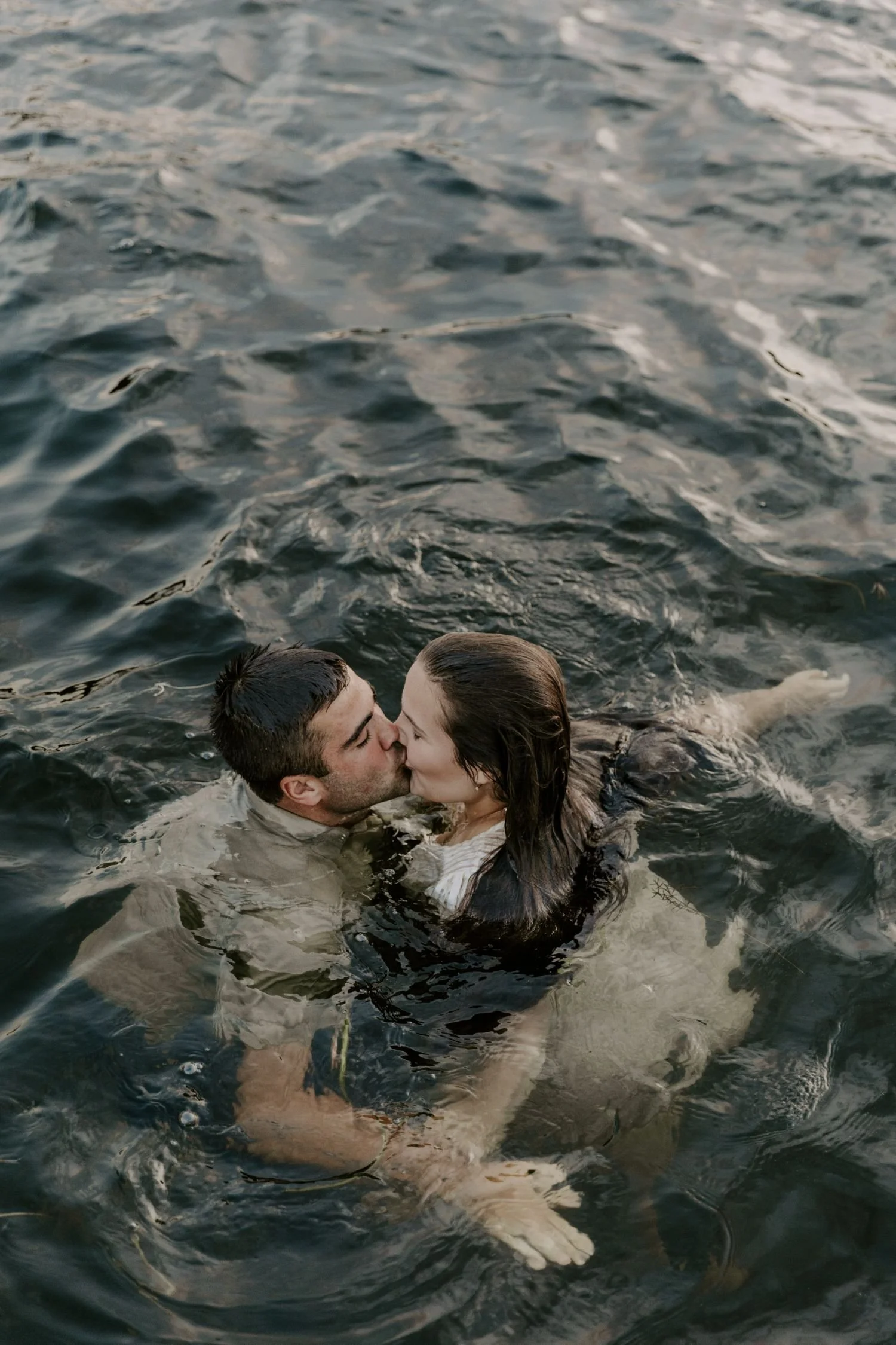 A couple is kissing in a body of water, with the man holding the woman close as they share a romantic moment during their couples photography package in Brockville Ontario.