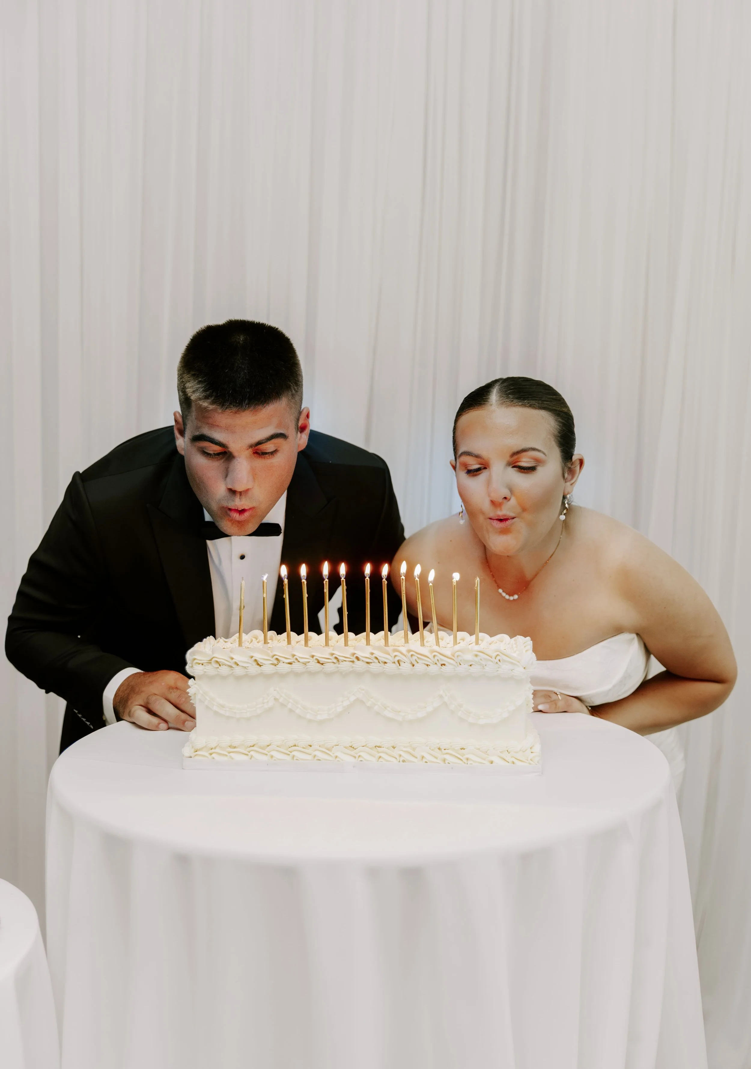 A bride and groom are blowing out candles on a wedding cake for their wedding photography package in Brockville, Ottawa, Ottawa Valley Ontario.