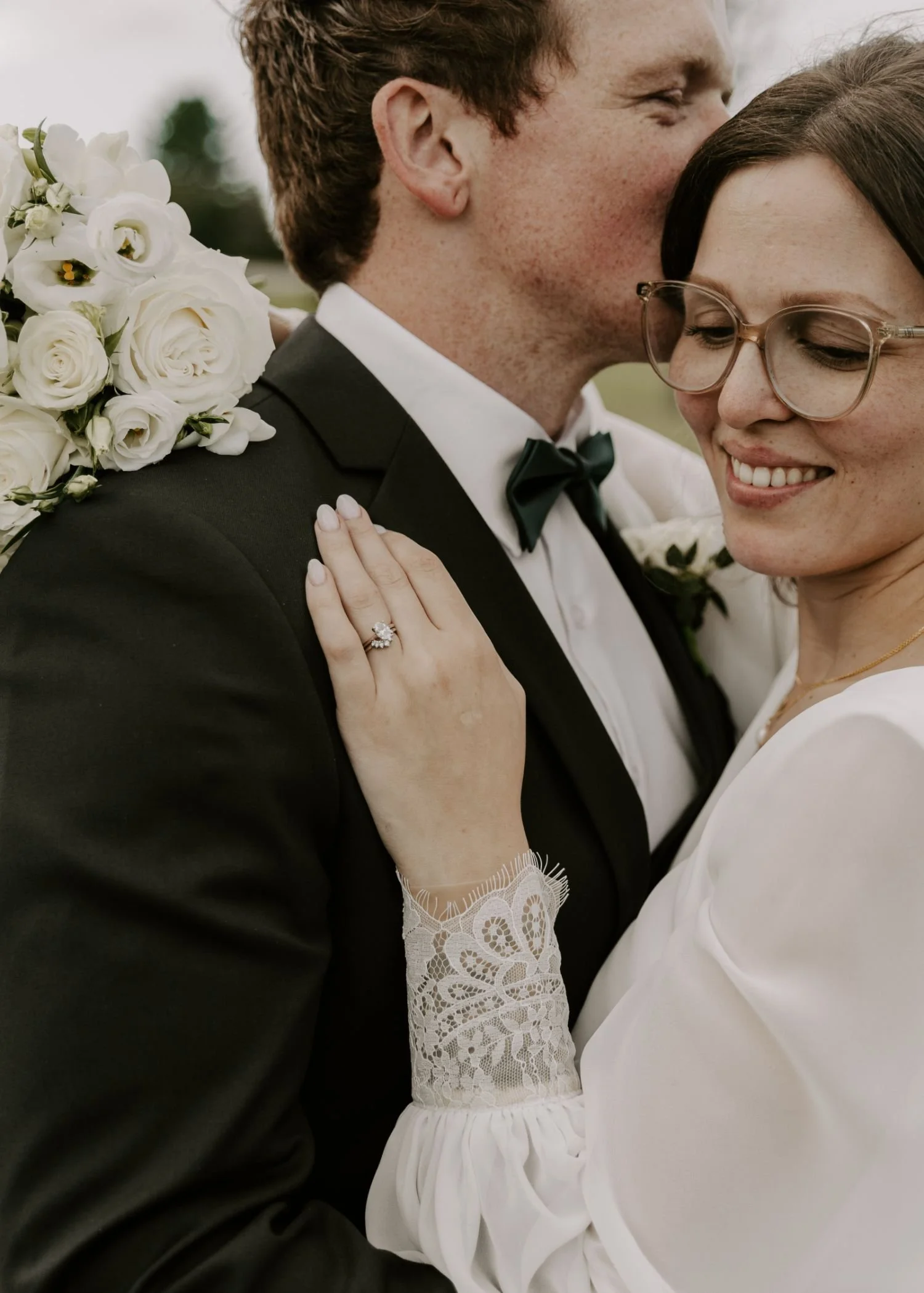 A close-up of a smiling couple at their wedding, with the man in a tuxedo and the woman in a white dress, showing a wedding ring on her finger for their wedding photography packages in Ottawa area.
