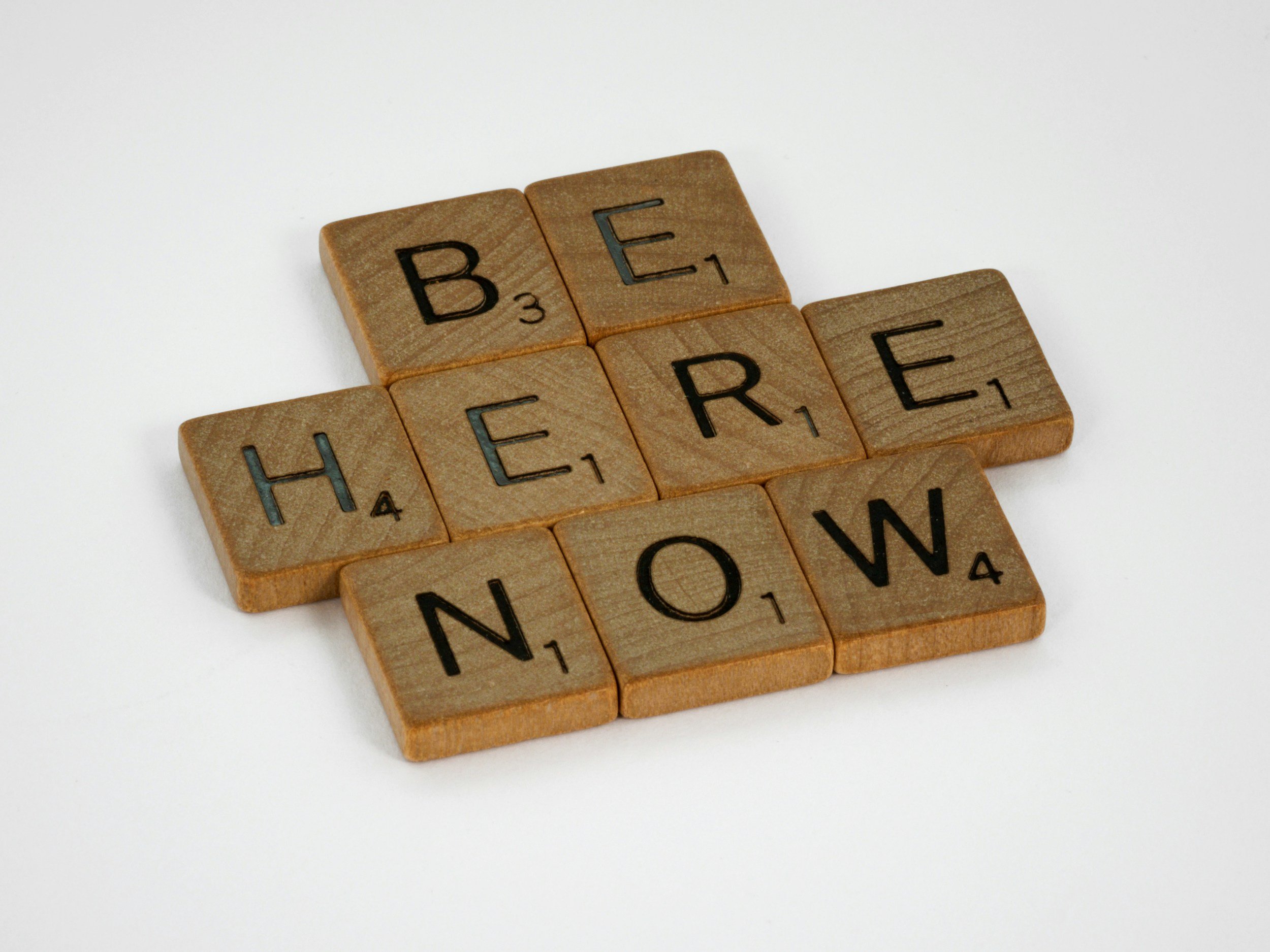 Scrabble pieces that spell out "Be Here Now" to support mindfulness and being in the present moment