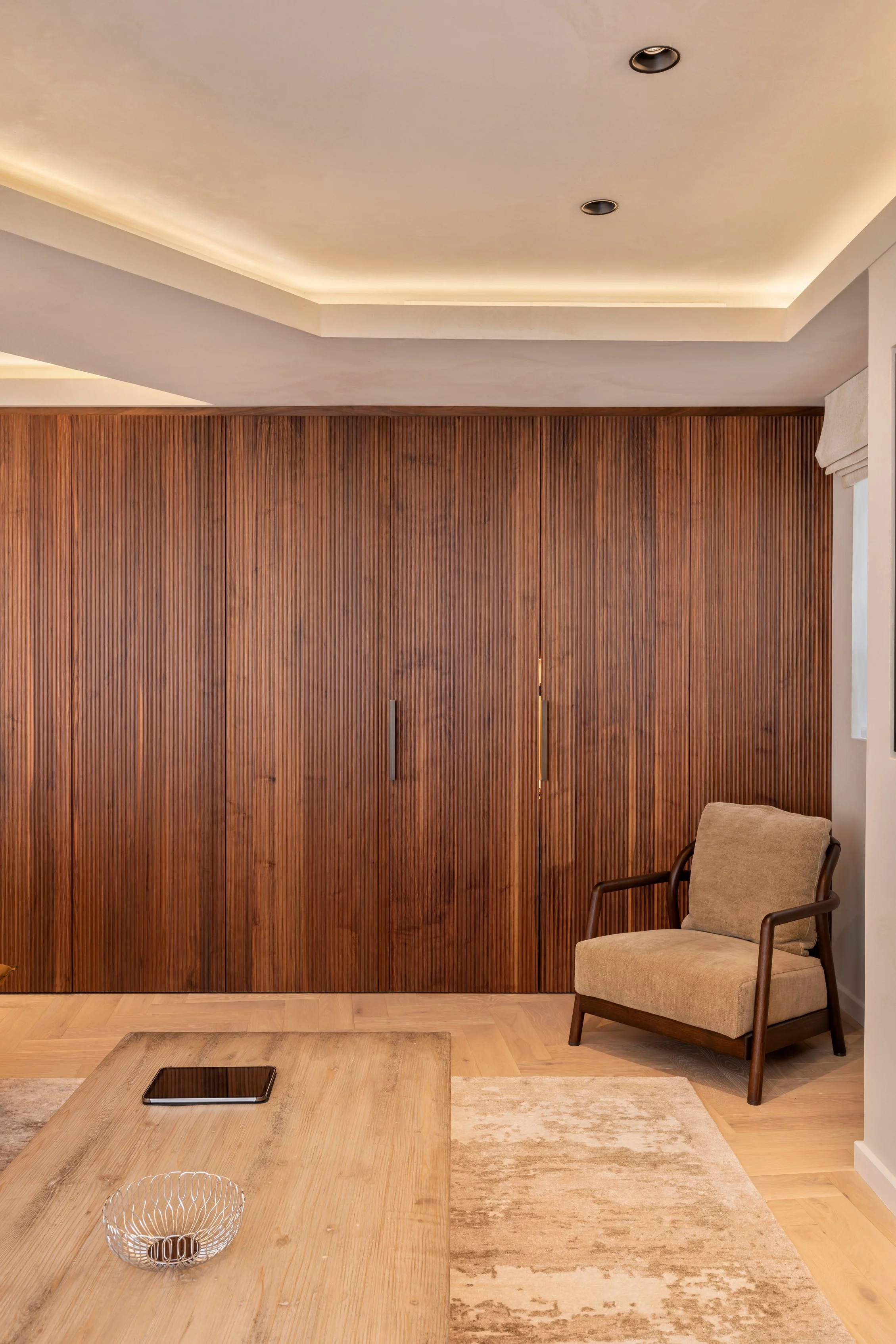 Living room with a wooden closet, beige chair, wooden coffee table, and a rug.