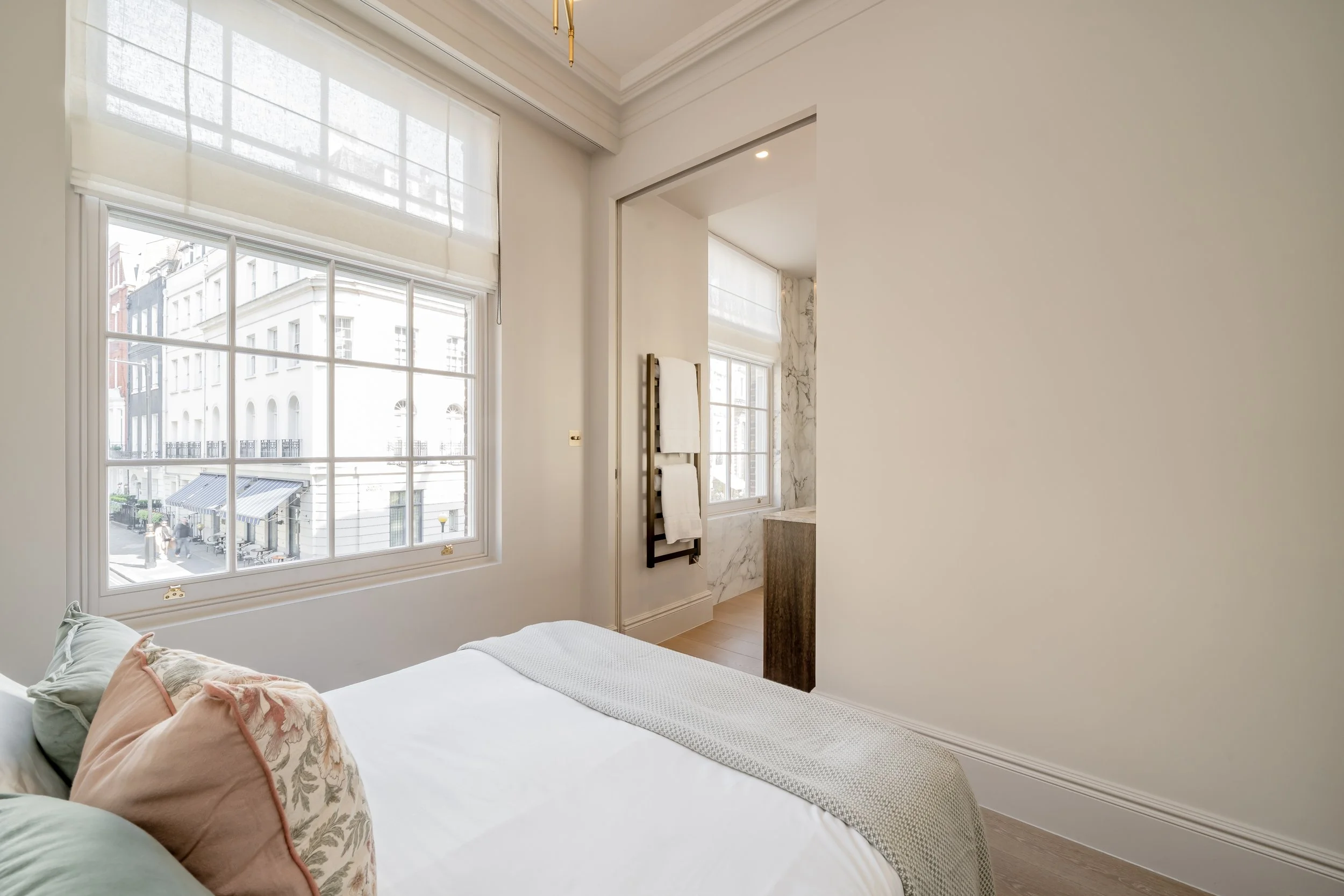 A bedroom with a large window, a bed with pillows, and a partial view of a bathroom with marble walls.
