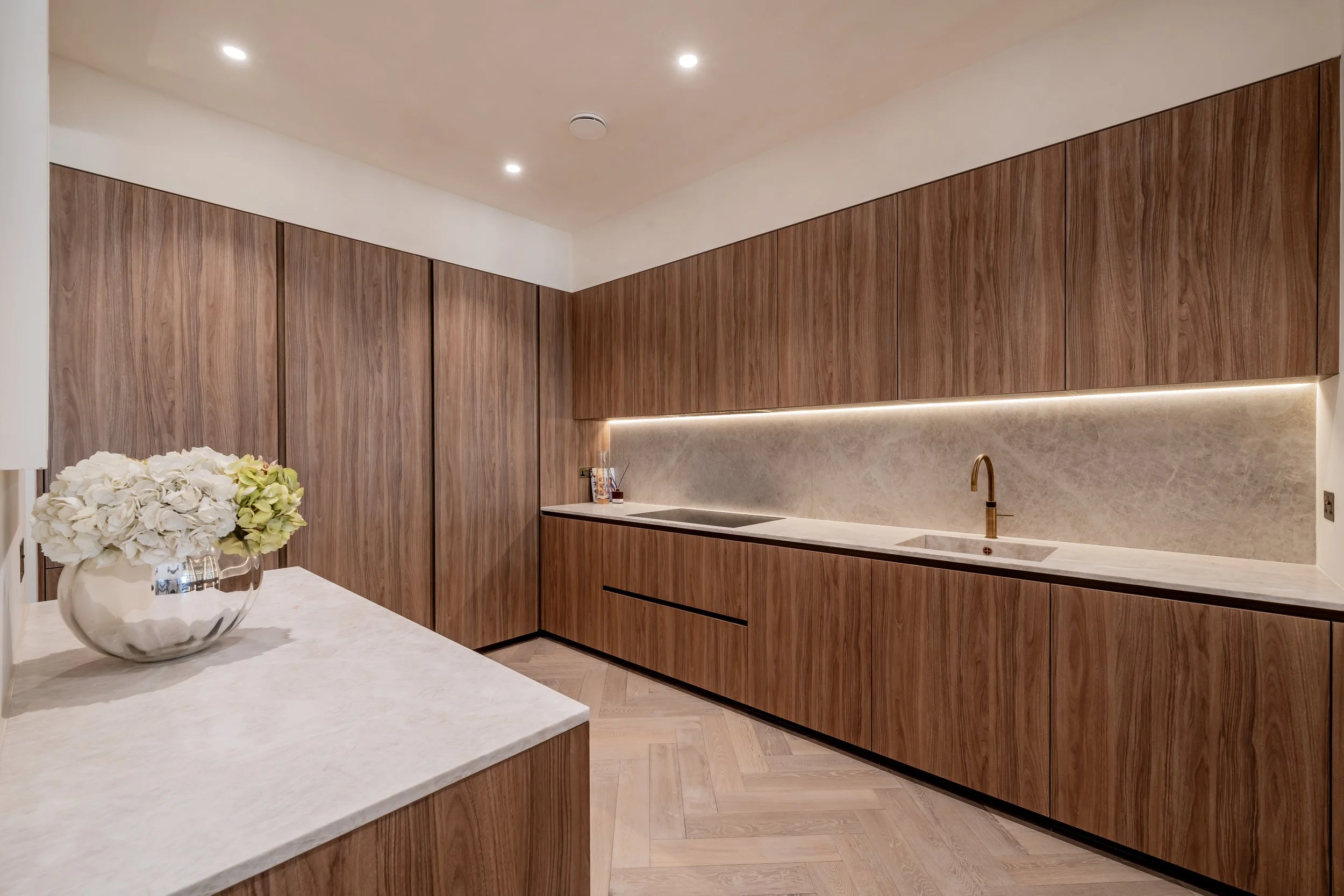 Modern kitchen with wood cabinets, marble countertops, gold faucet, and potted flower on island.