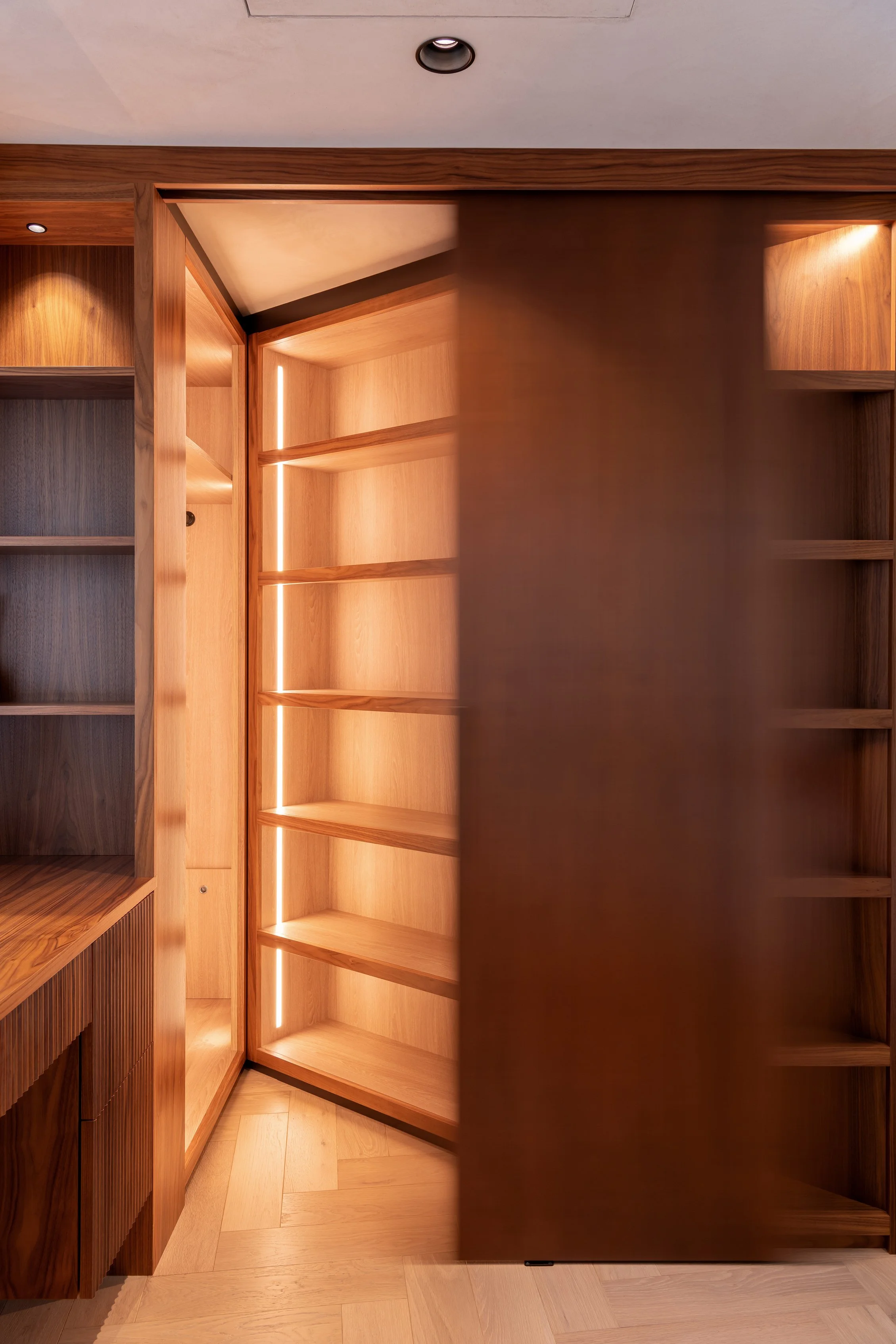 View of wooden built-in shelves and cabinets in a room, with a sliding door partially open, revealing empty shelves.