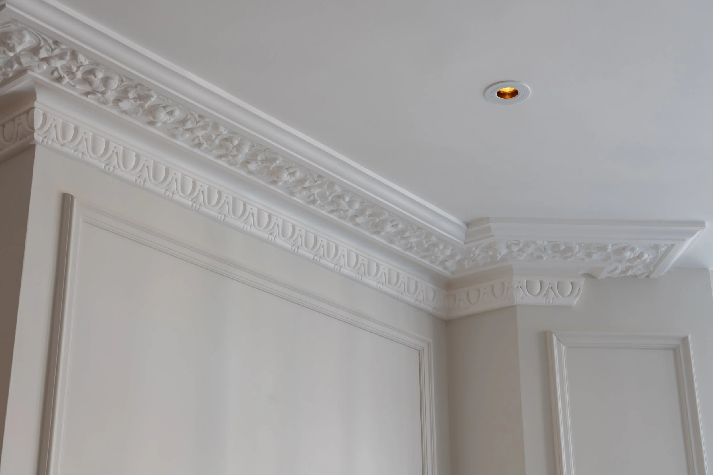 White ceiling and wall with ornate crown molding and decorative trim in a fancy room.
