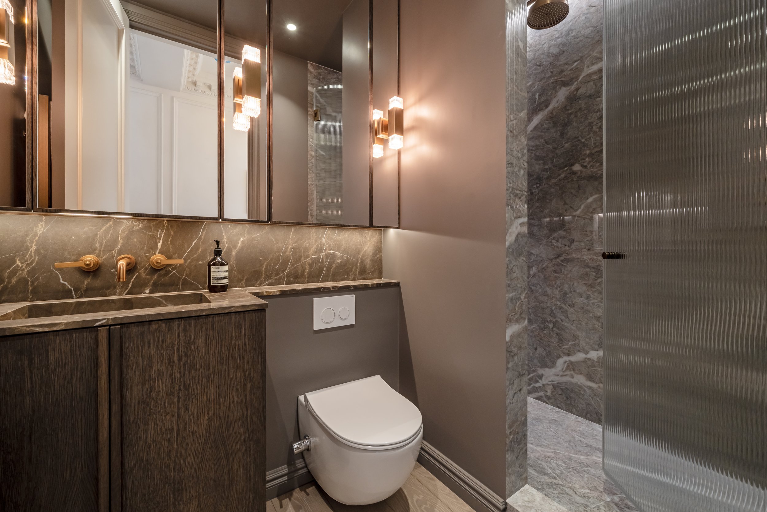 Modern bathroom with a marble countertop, a mirror, a wall-mounted toilet, and a shiny textured metal shower door.