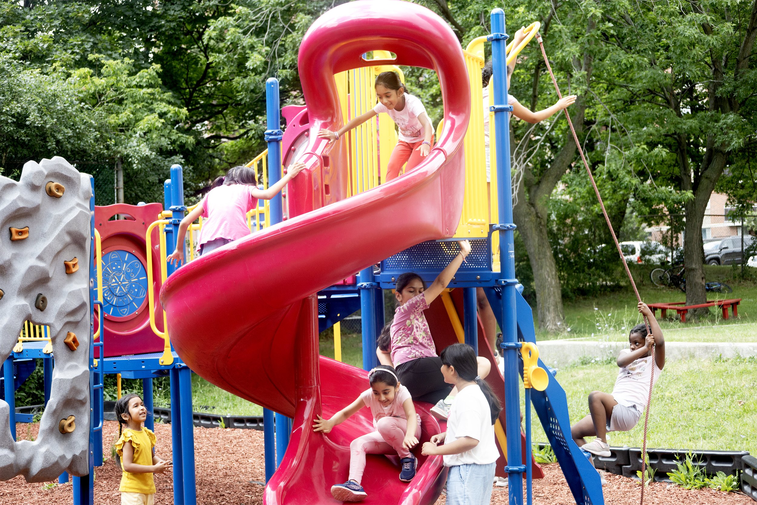 Summer camp children playing at playground under staff supervision between activities.