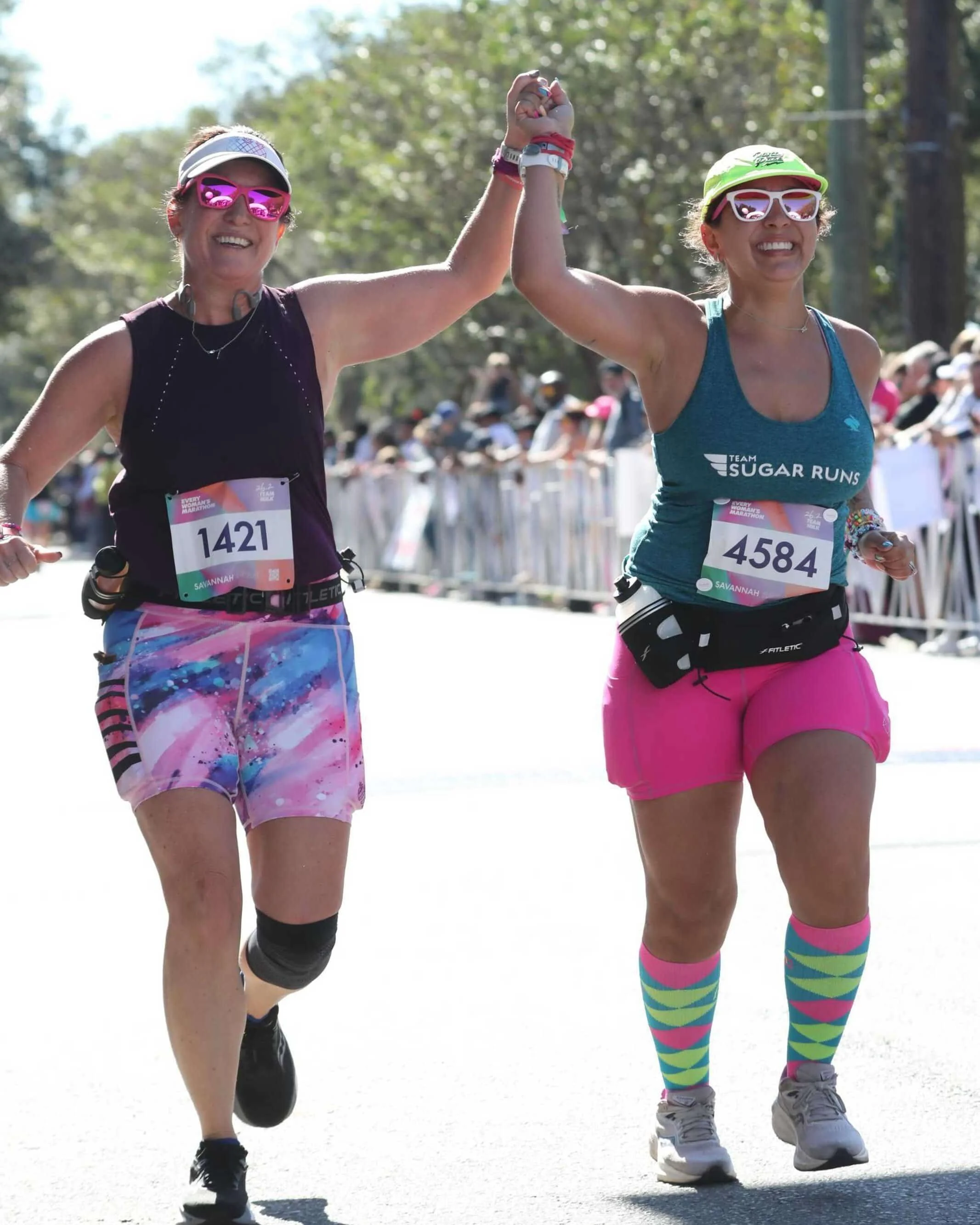 Two women holding hands while heading to the finish line of Every Woman's Marathon