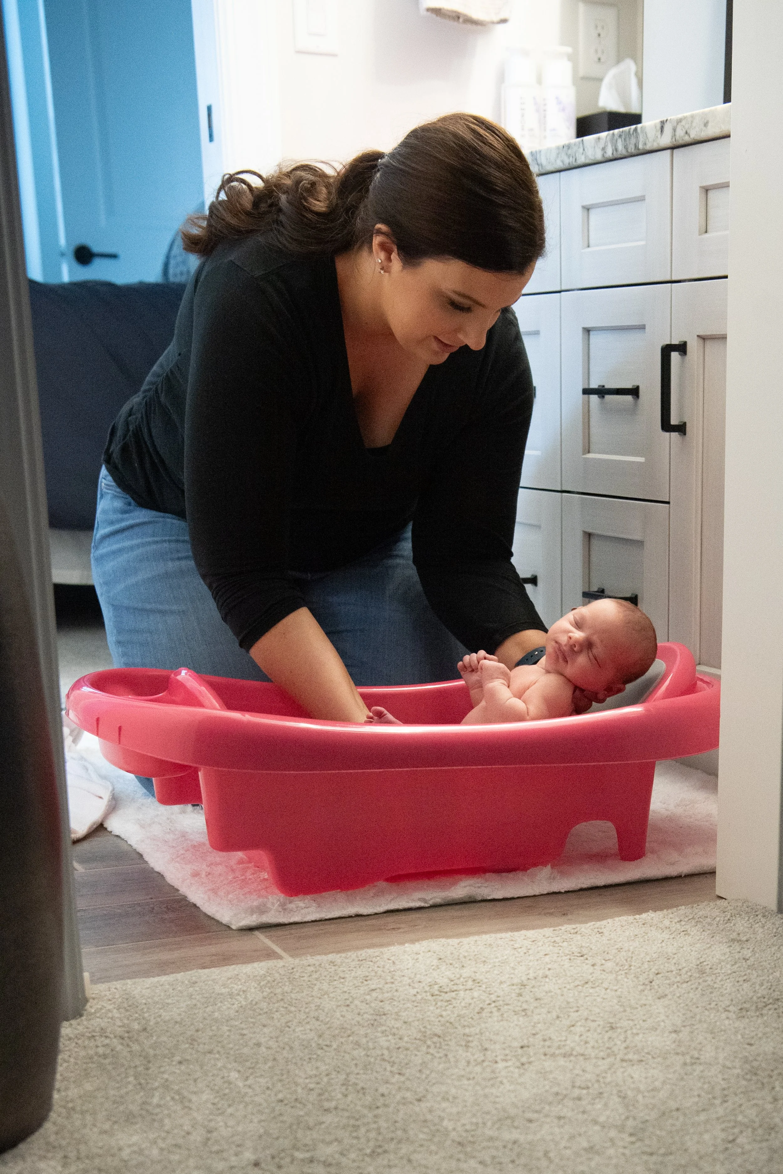 Newborn Care Specialist bathing baby in pink bath tub