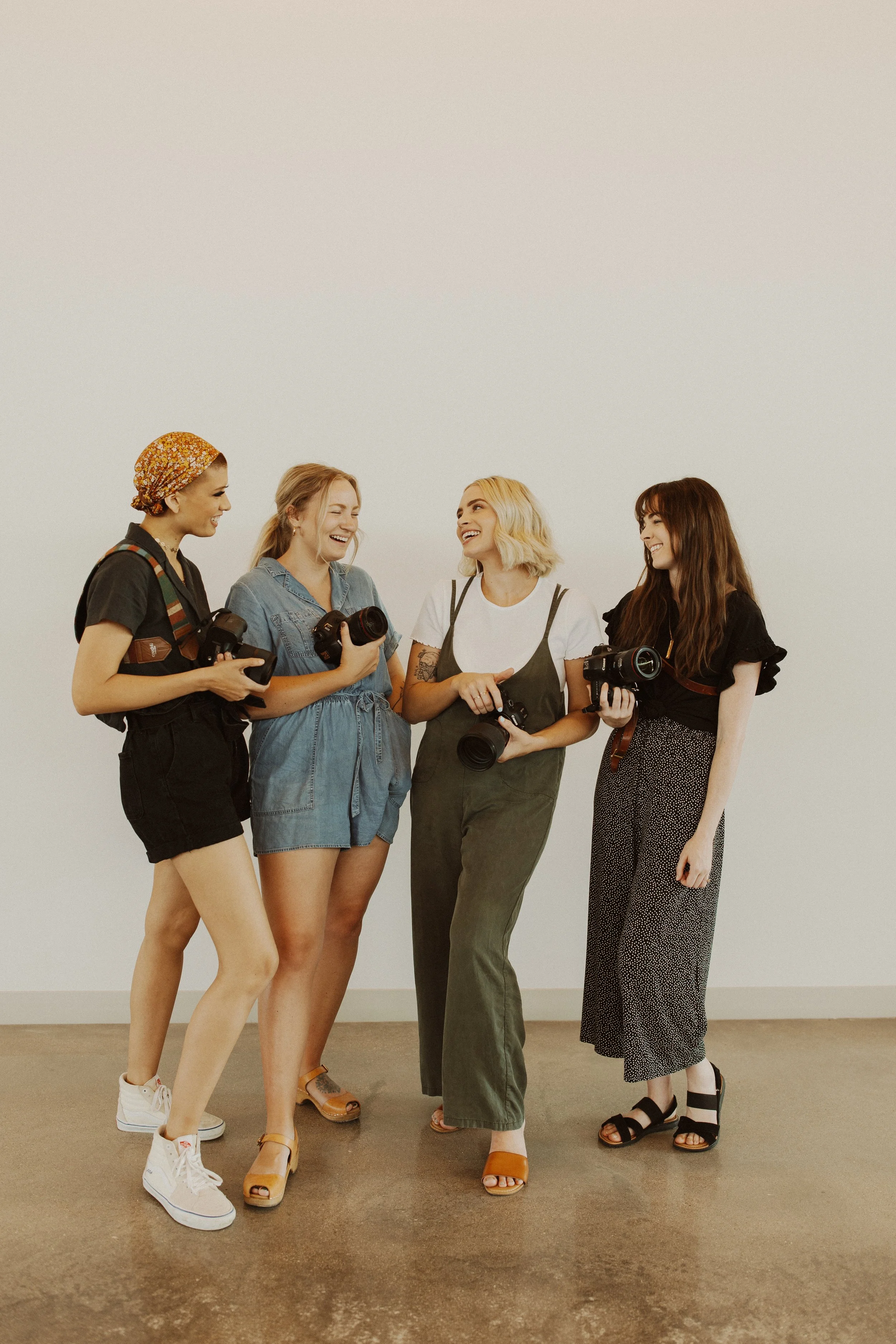 Grace Troutman's photography team standing together, holding cameras, smiling and laughing in an indoor setting with a plain white wall background.