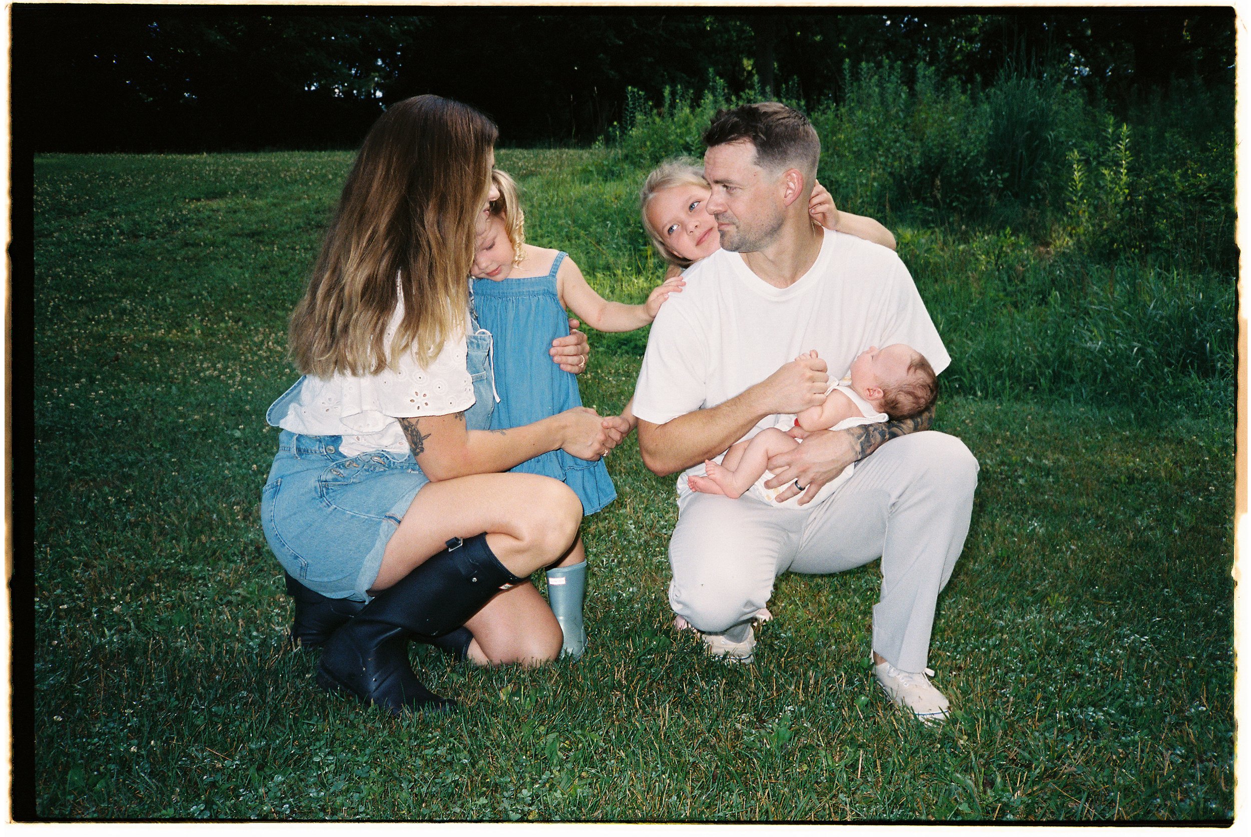 Grace Troutman's Family on a grassy field during the summertime with lush trees in the background.