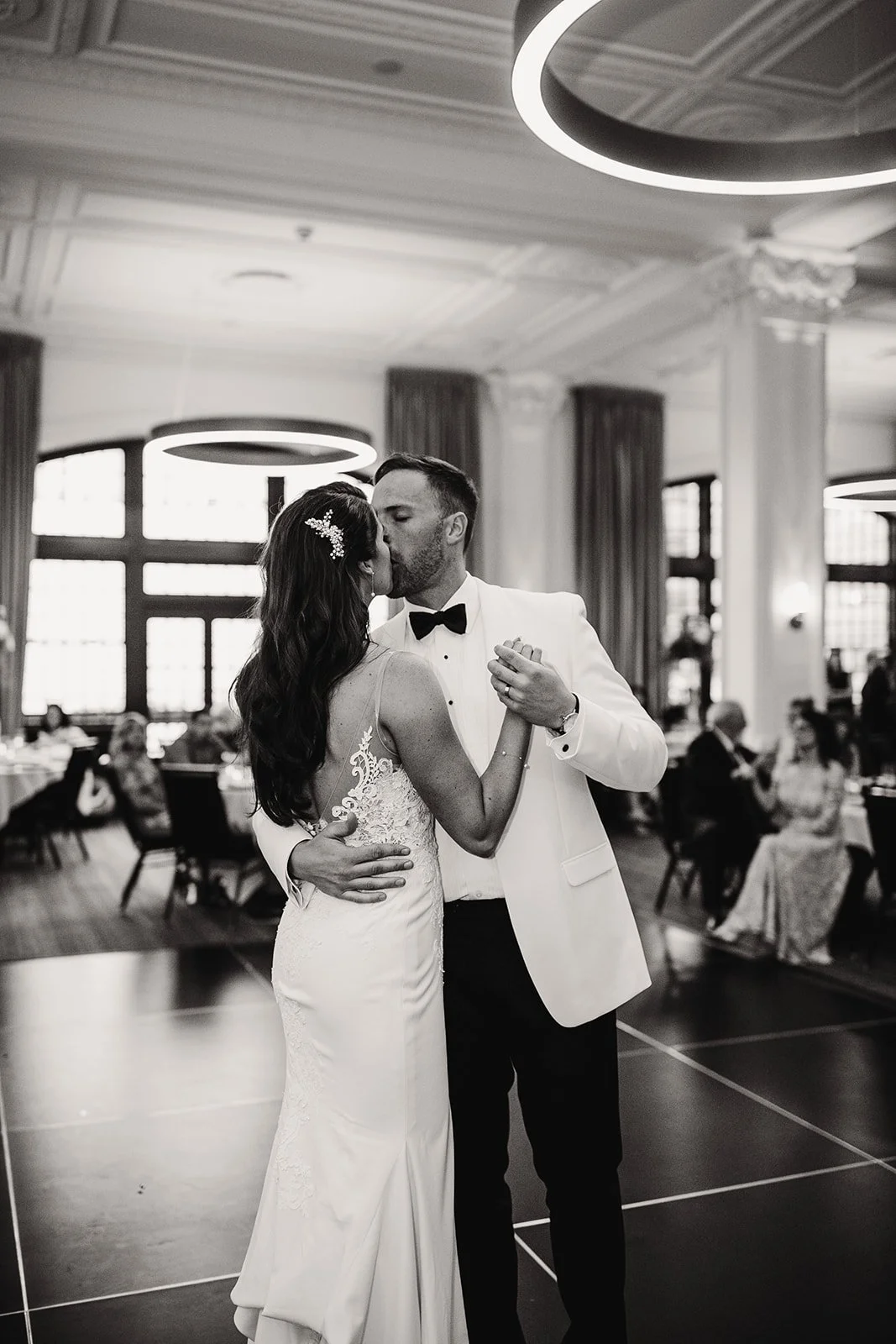 A bride and groom share their first dance in an elegant Tea Room venue, with guests seated at tables in the background.