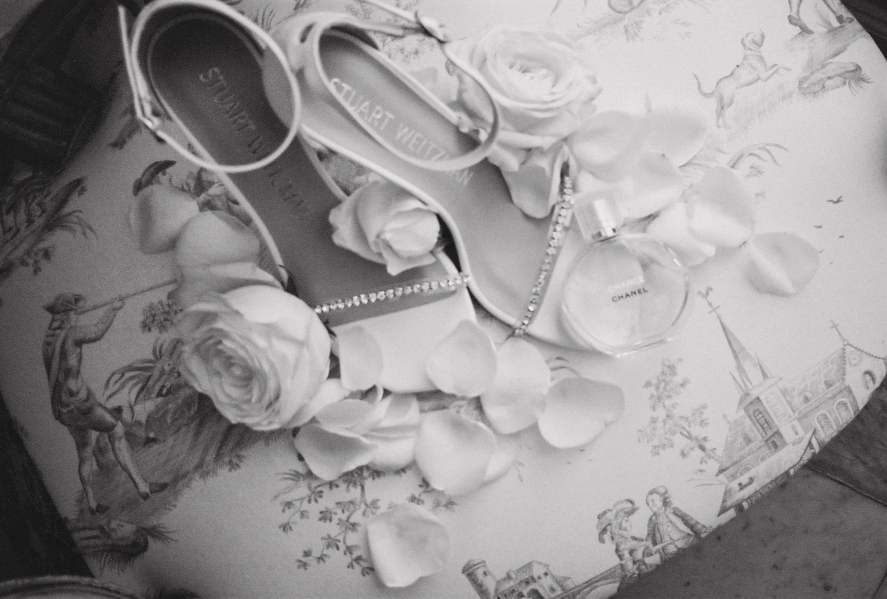 A flat lay of perfume bottles, jewelry, and rose petals on a patterned surface with illustrations of children and a church.