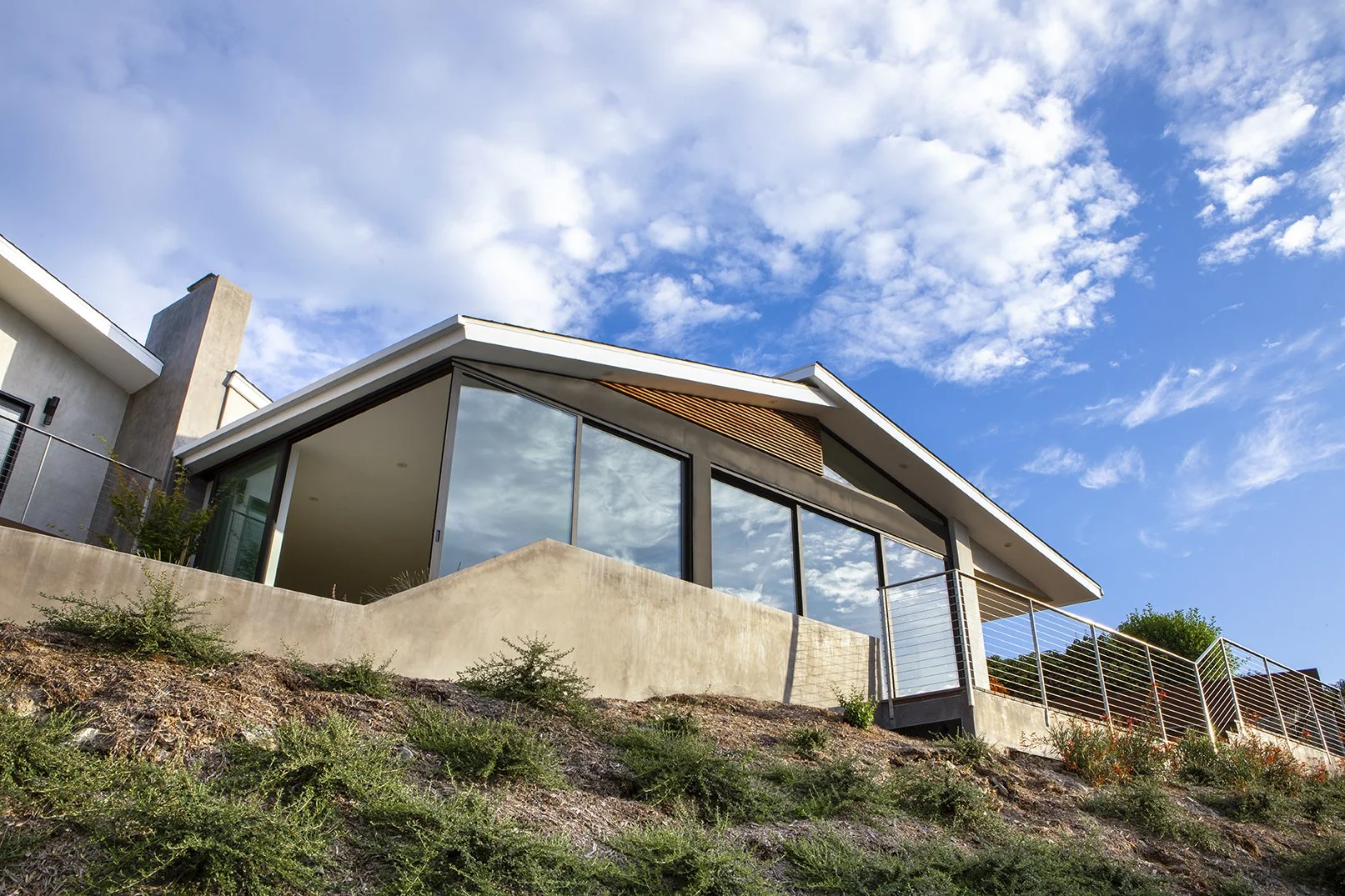 Modern house with large glass windows on sloped hillside terrain and a blue sky with scattered clouds in palos verdes.