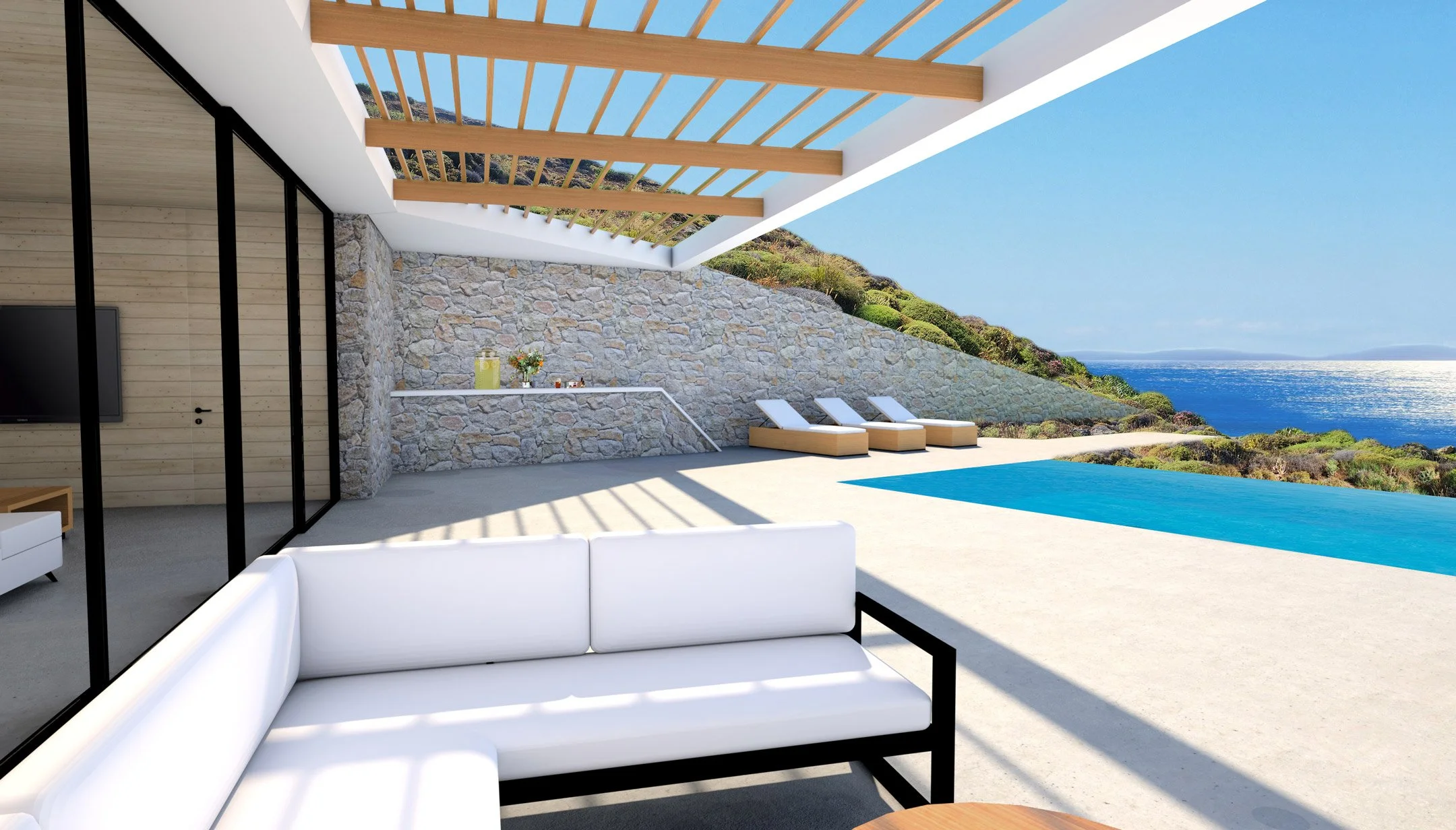Modern outdoor patio area with white seating, a stone wall, a pool, lounge chairs, and a view of the ocean and hillside.