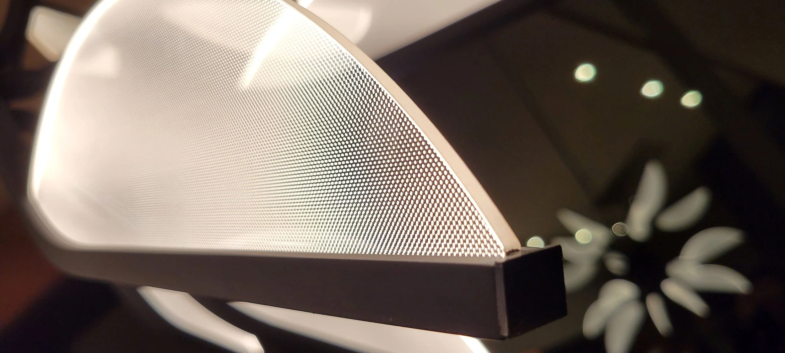Close-up of a modern hanging light chandelier with a white mesh grille and black base, illuminated by ambient lighting.