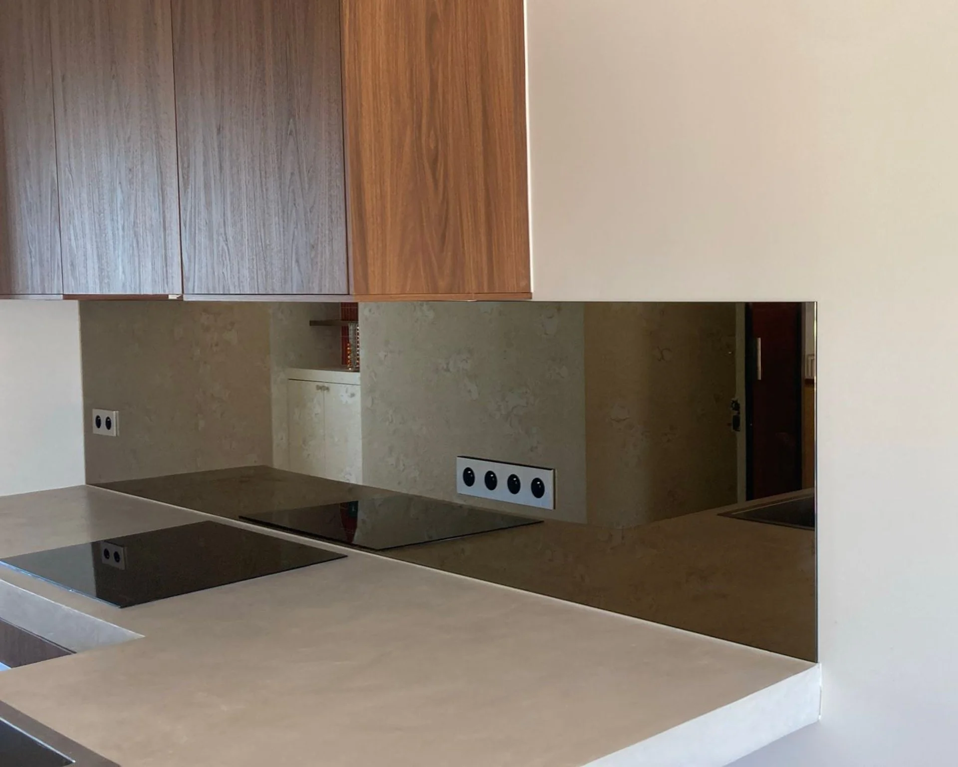 Cuisine moderne avec plans de travail beige, murs en pierre beige, et appareils électroménagers noir intégrés.
