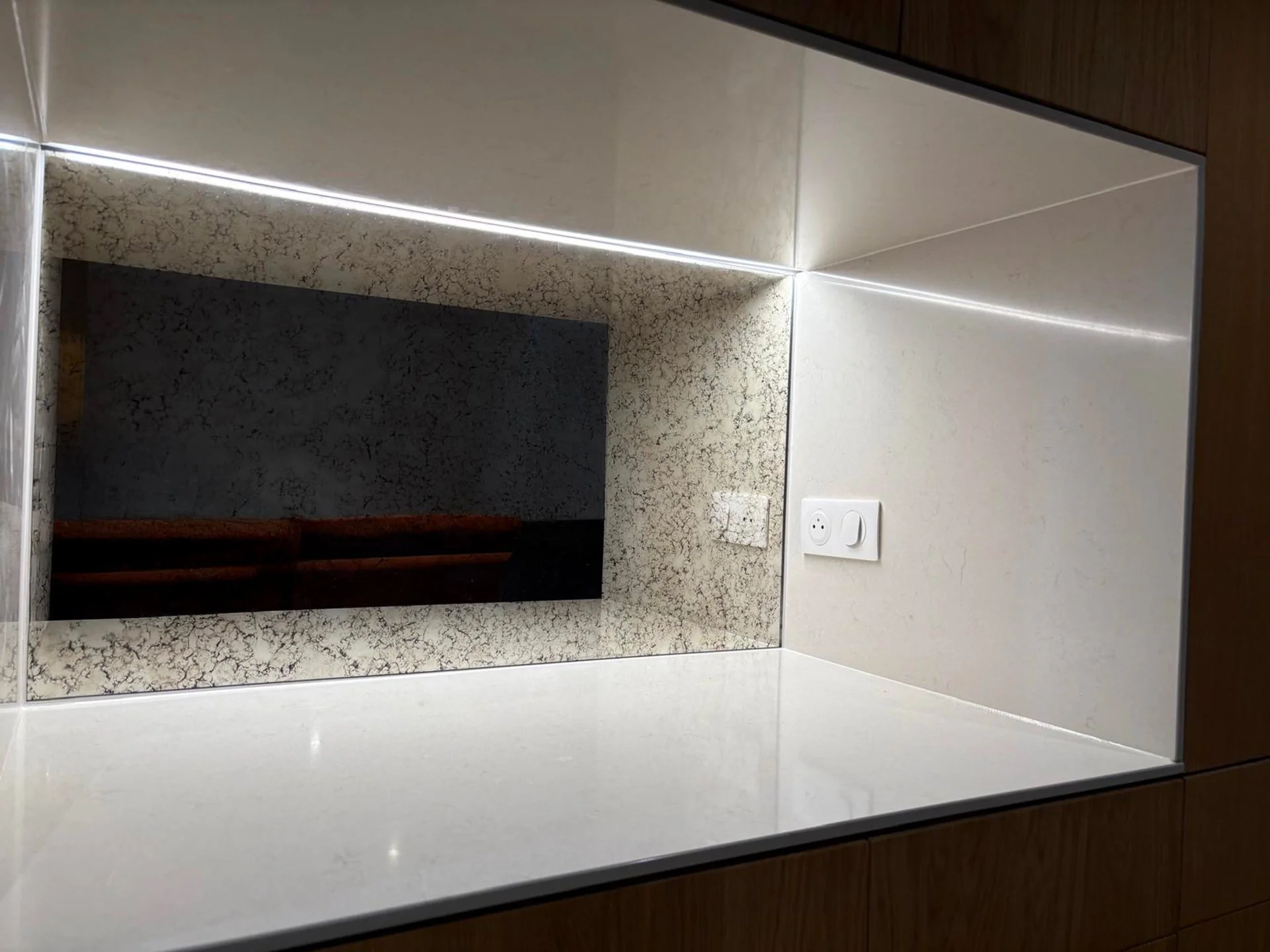 Miroir rectangulaire au-dessus d’un plan de travail en pierre blanc avec prises électriques, dans une cuisine moderne.