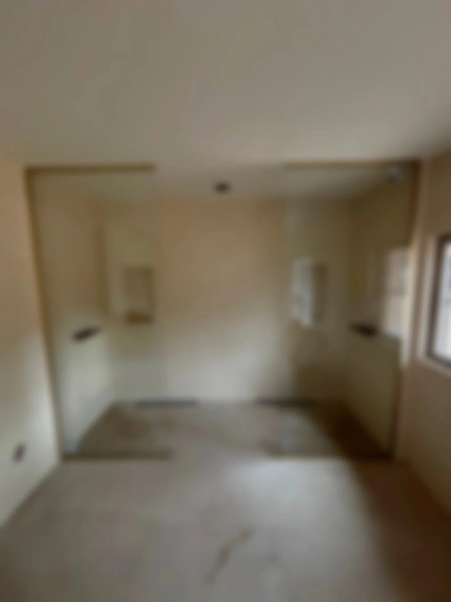 Une pièce vide avec murs beige clair, un plafond blanc, un sol beige, une fenêtre à droite, et deux petites fenêtres ou ouvertures au fond.