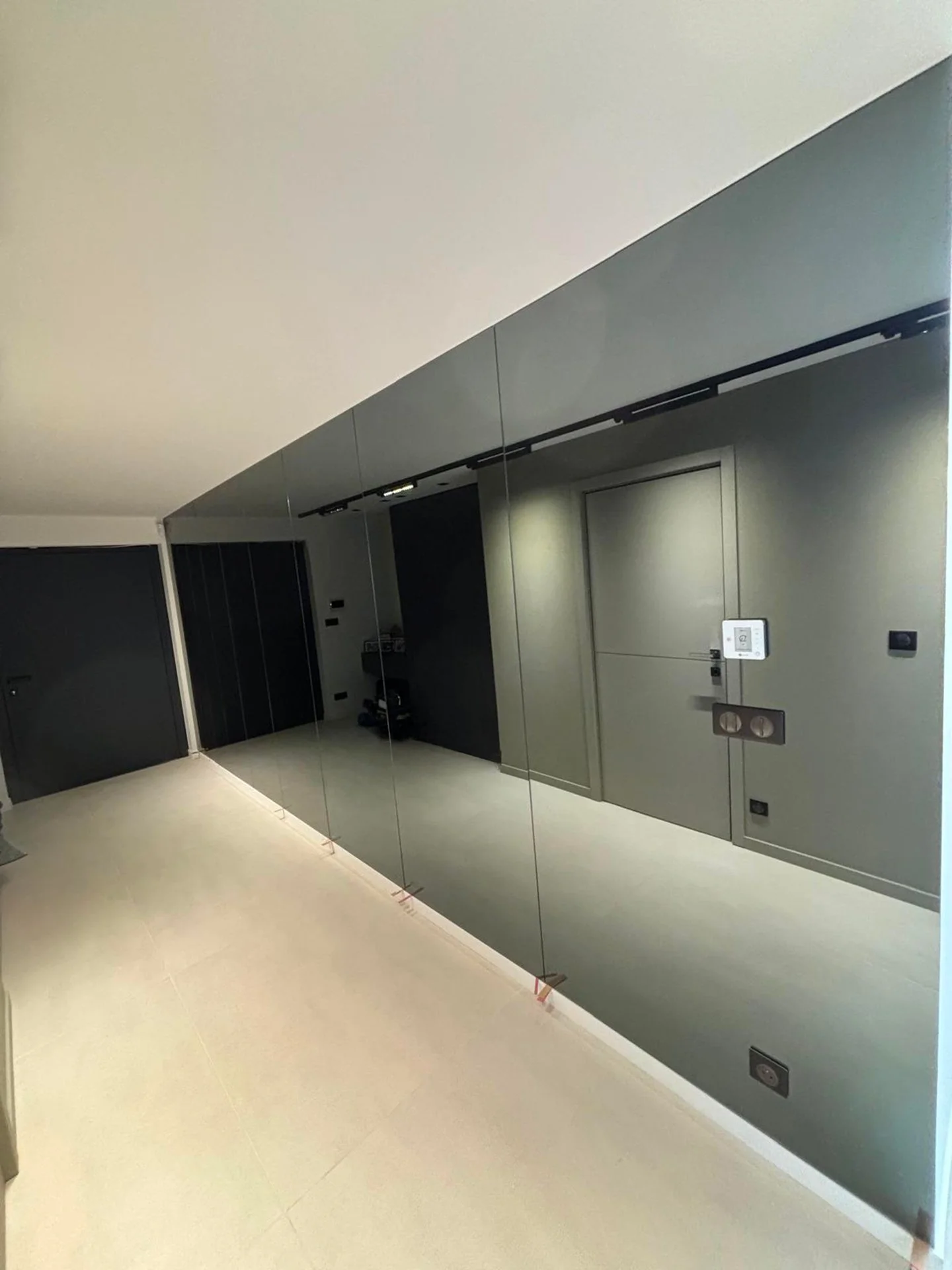 Miroir mural dans une pièce moderne, avec des prises électriques et des interrupteurs sur le mur gris, et un sol en carrelage clair.