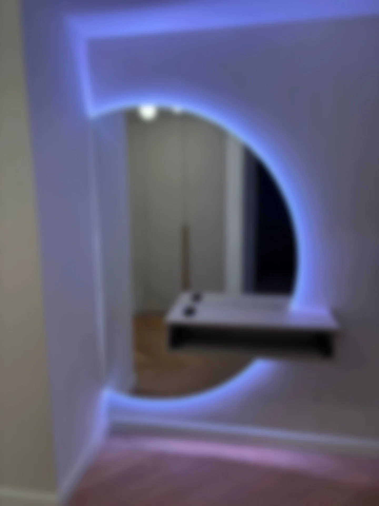 Une pièce sombre avec un miroir rond encadré de lumière bleue.