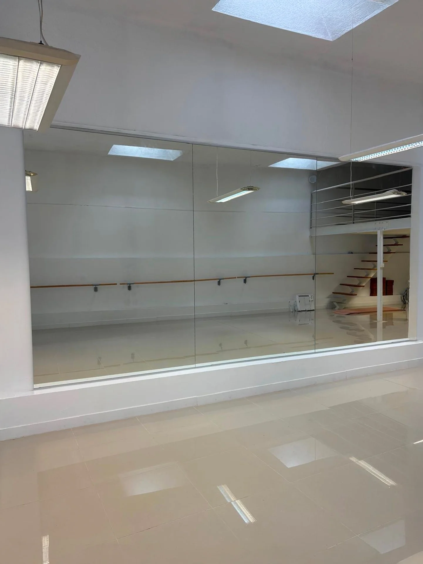 Salle de danse vide avec miroir mural, barres de ballet et escaliers en arrière-plan.