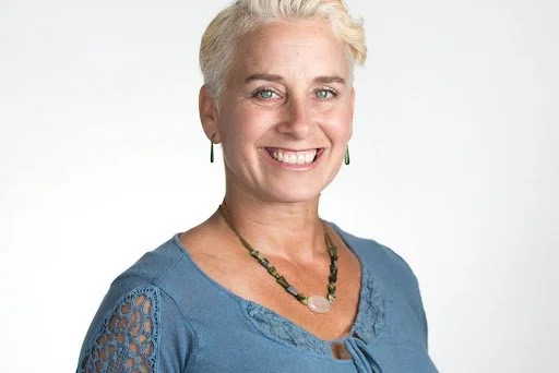 Head shot of teacher Joy Ravelli. She is blonde with blue eyes, wearing a blue top and smiling at the camera