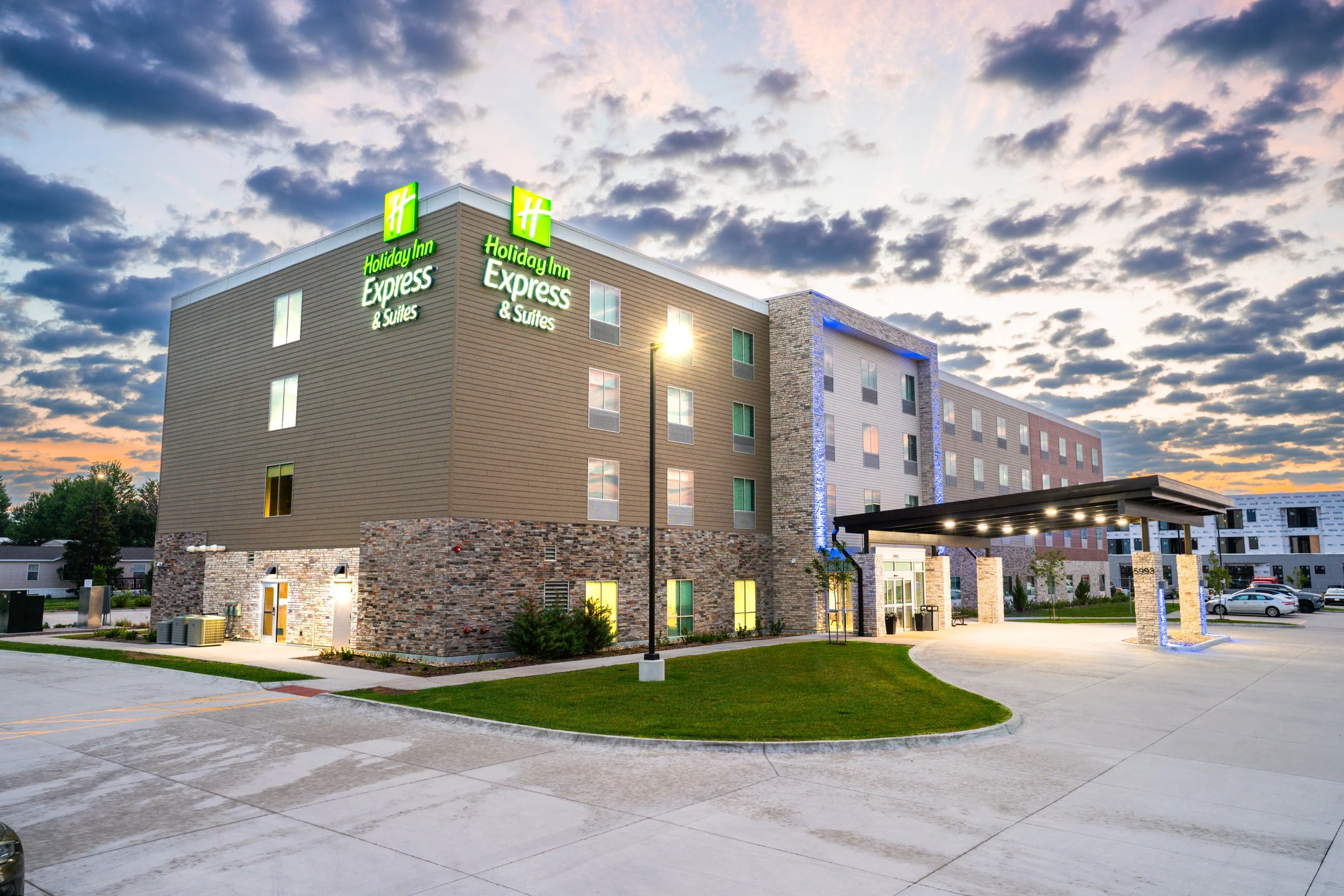 Exterior of a Holiday Inn & Express hotel at sunrise with a purple sky, white building, covered entrance, and parking area.