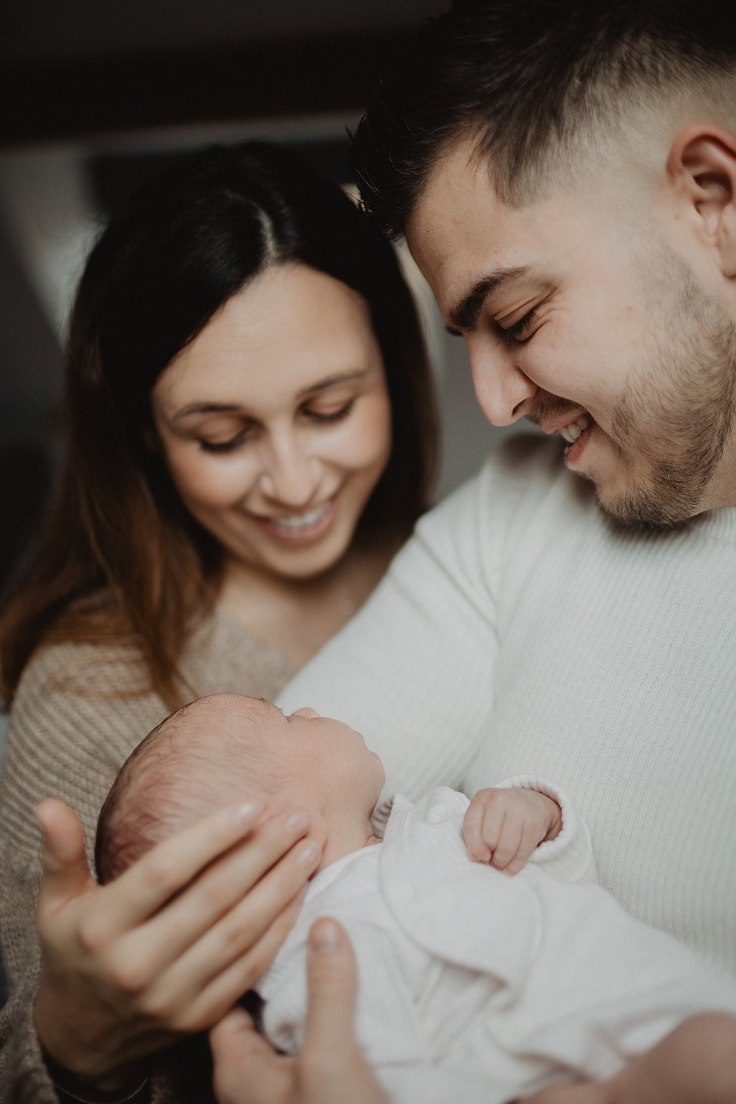 Parents standing close whilst holding newborn baby during a newborn photography session.