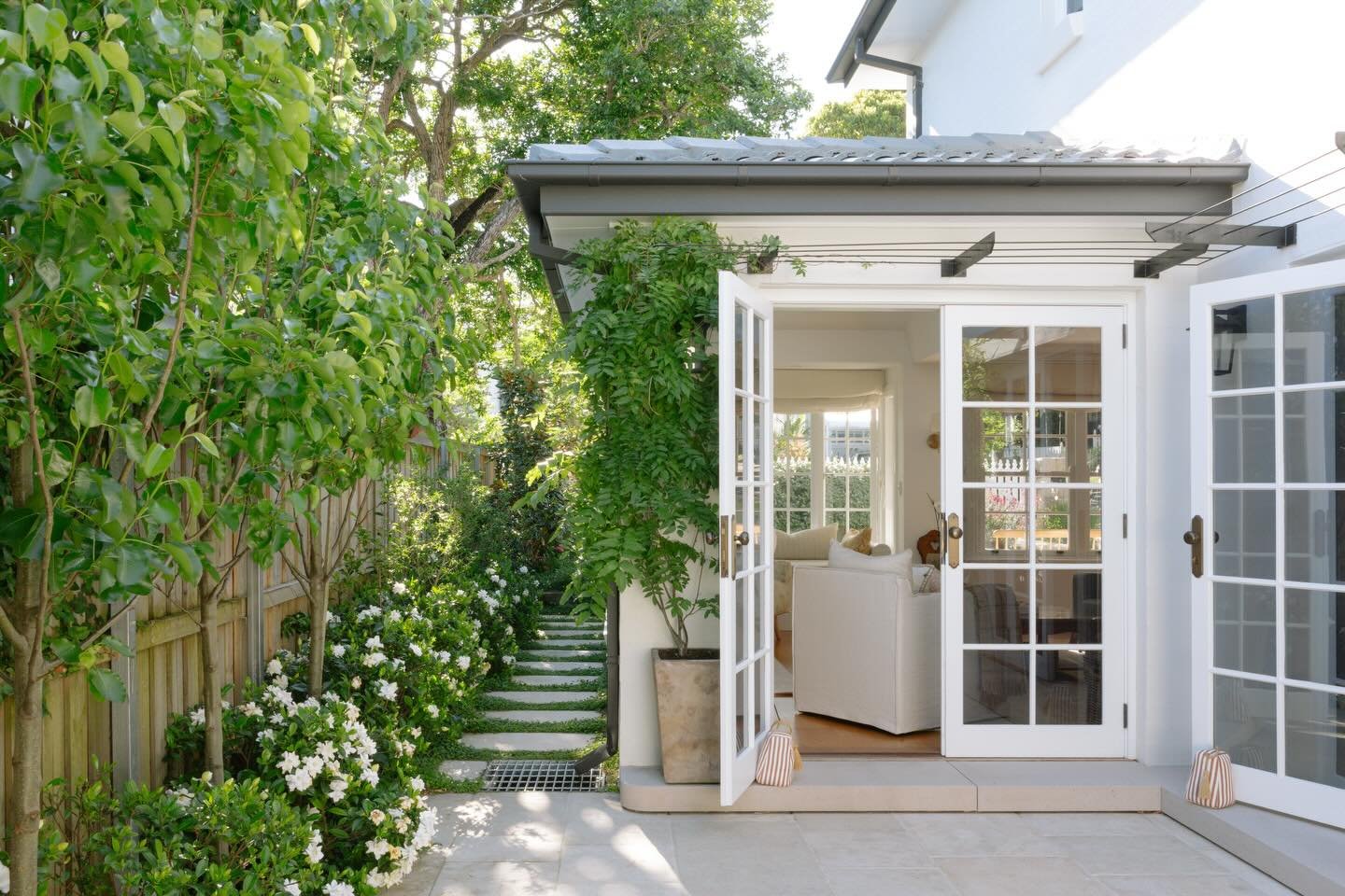 French doors opening up to a limestone paved courtyard framed by Pear trees &amp; Gardenia under planting.
