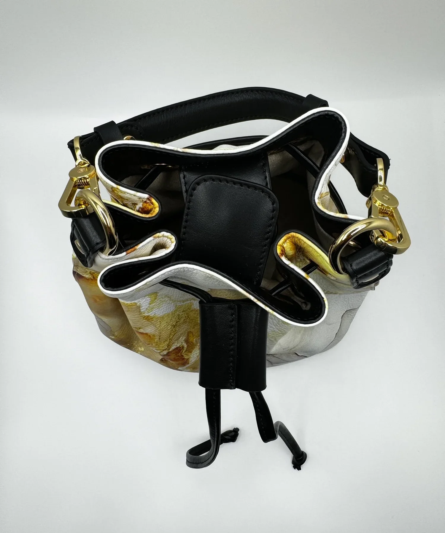 A close-up photo of a gold and white marble-patterned bucket bag with a black drawstring closure.