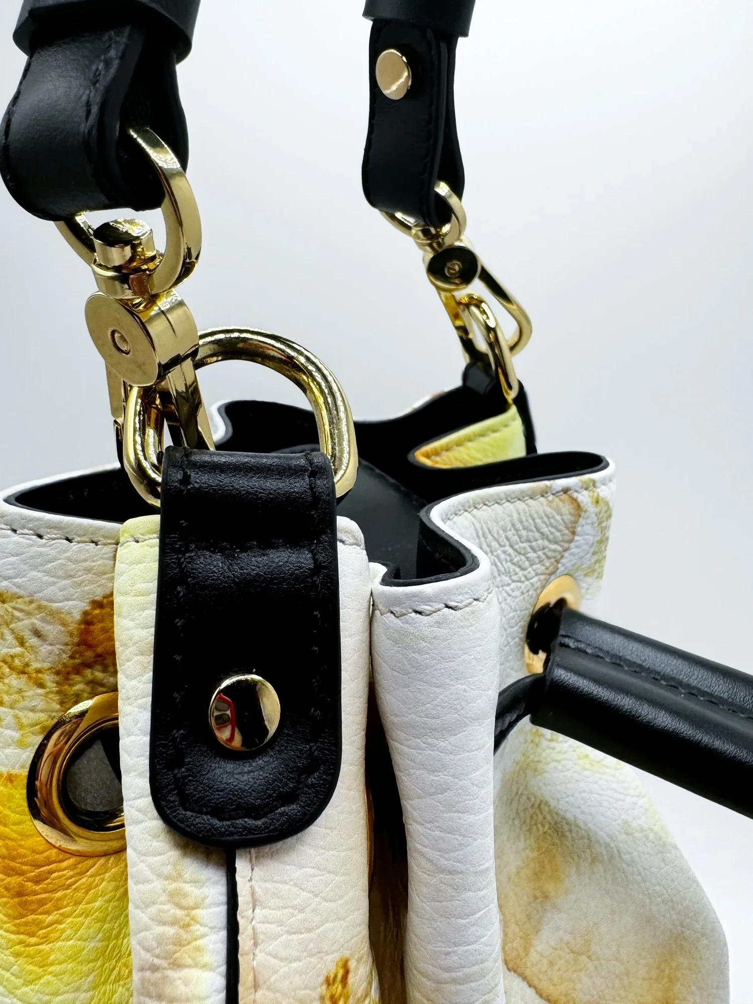 A close-up photo of a gold and white marble-patterned bucket bag with a black drawstring closure.