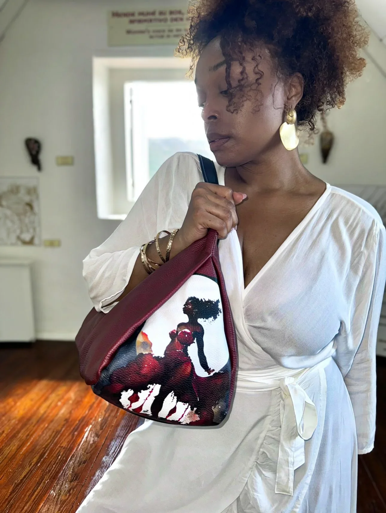 A model holding a maroon-colored leather shoulder bag with a unique graphic print of a moon goddess connected with her cycle..