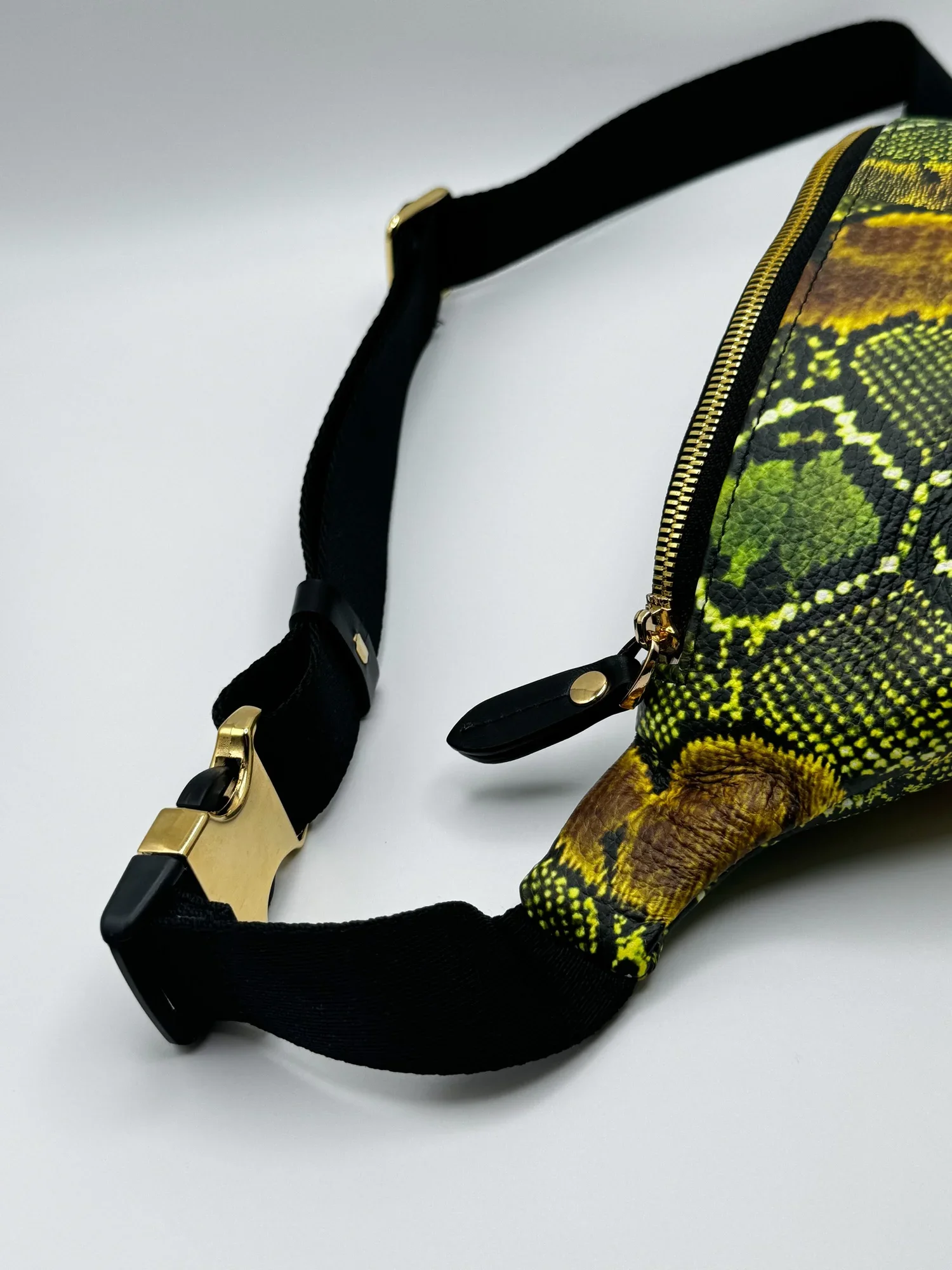 Close up photo of a green and black textured snakeskin print fanny pack, on a white surface.