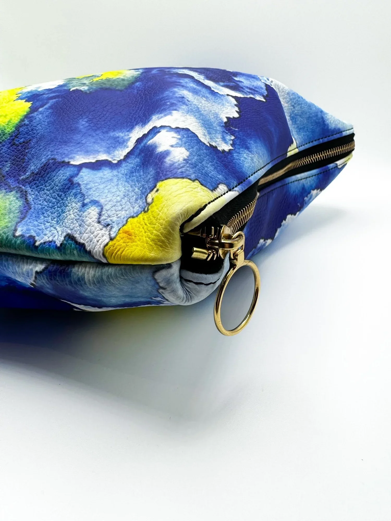 A close up photo of a large yellow, blue and white leather clutch with a gold circle pull and gold zipper, on a white background.