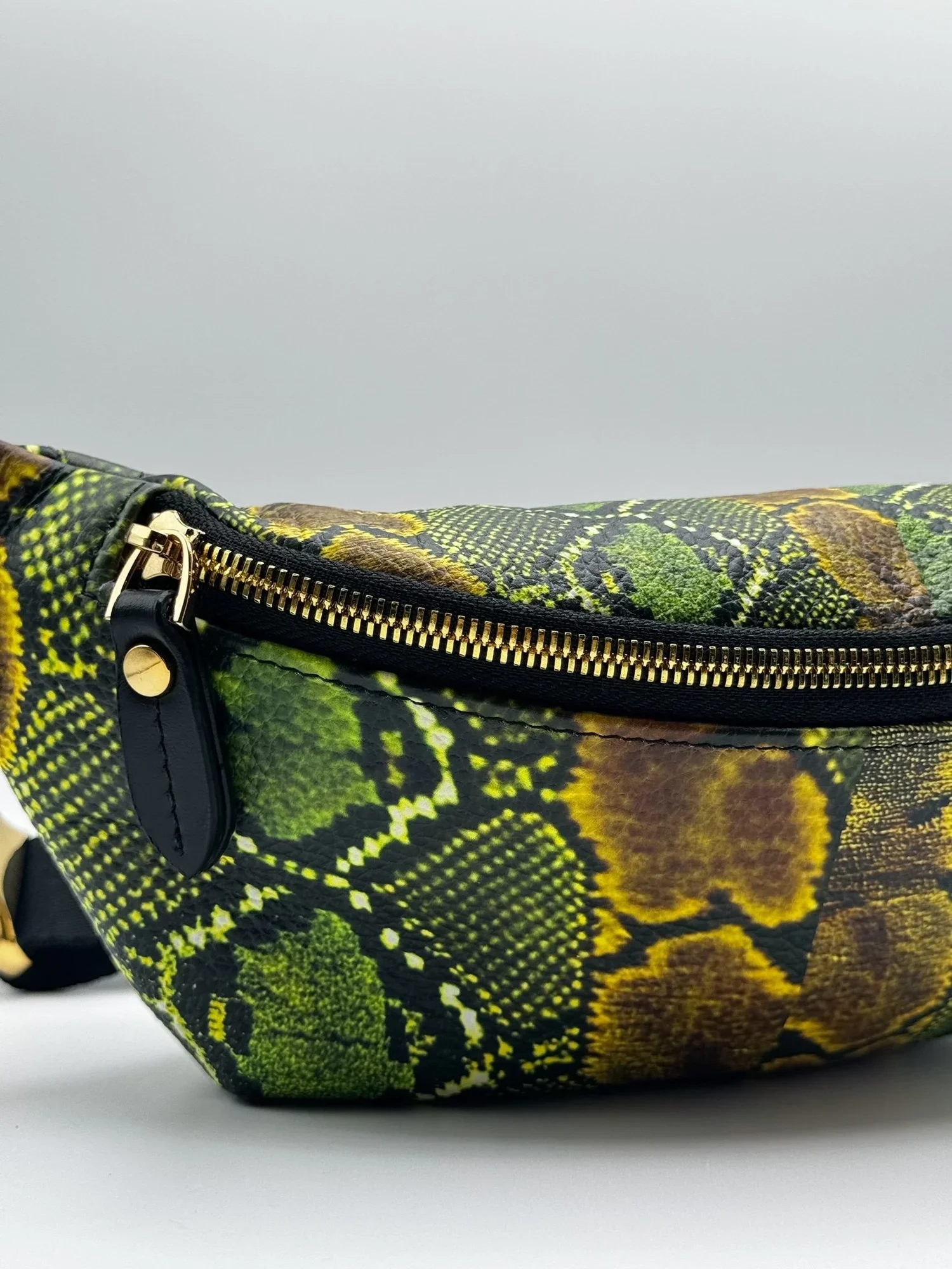 Close up photo of a green and black textured snakeskin print fanny pack, on a white surface.