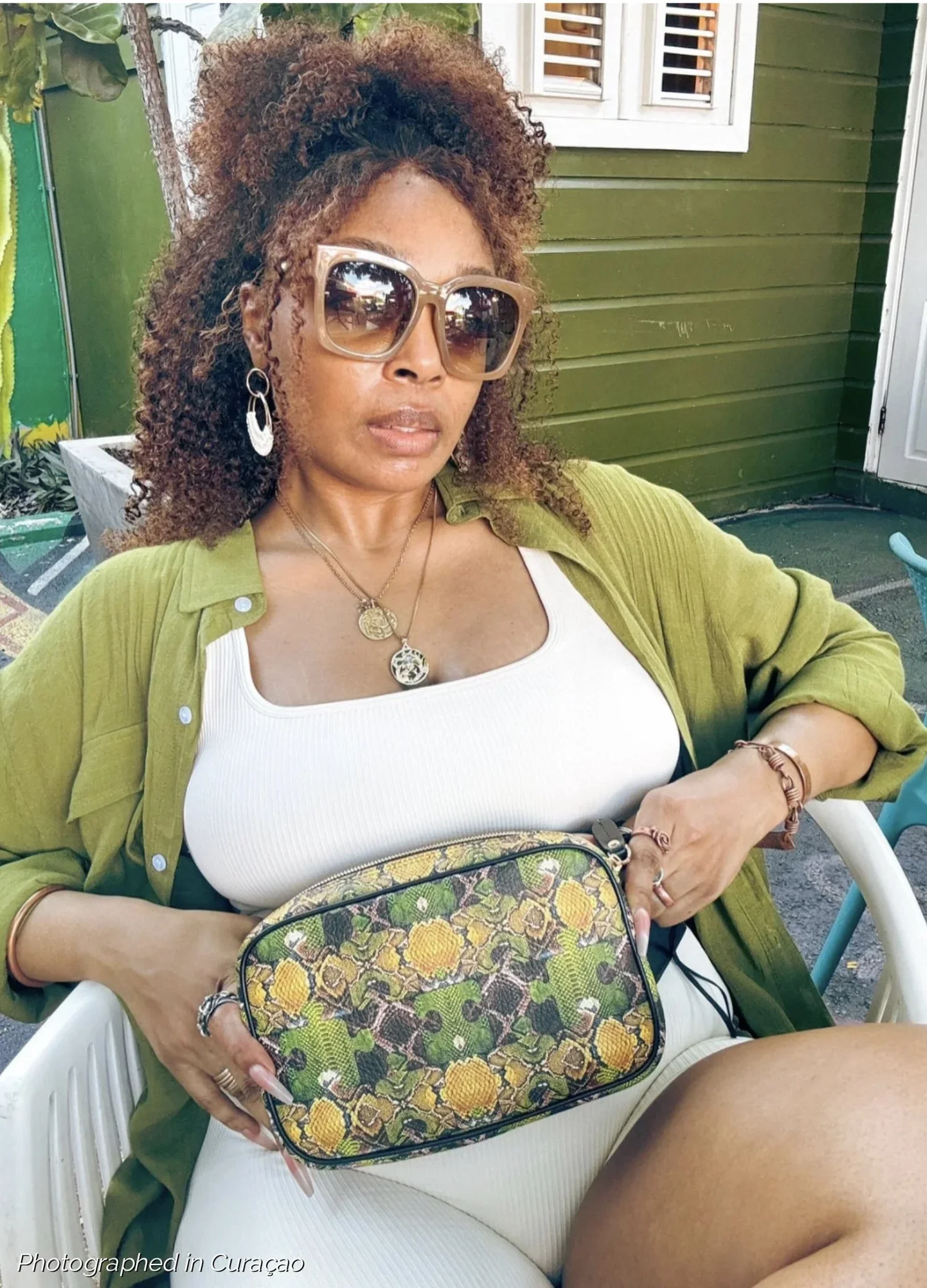 A model wearing a large "Mosaic" belt bag with a signature serpent patchwork pattern made of textured Nappa leather. The model wears a cream colored top and shorts set, with an army green buttoned-down collared shirt.