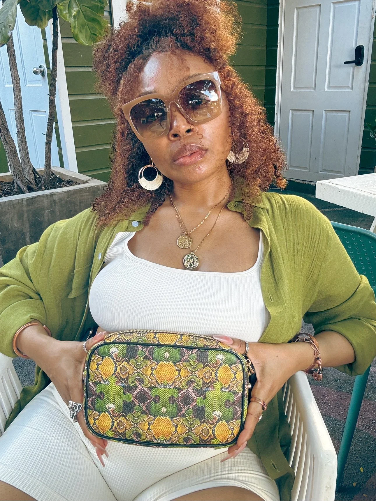 A model wearing a large "Mosaic" belt bag with a signature serpent patchwork pattern made of textured Nappa leather. The model wears a cream colored top and shorts set, with an army green buttoned-down collared shirt.