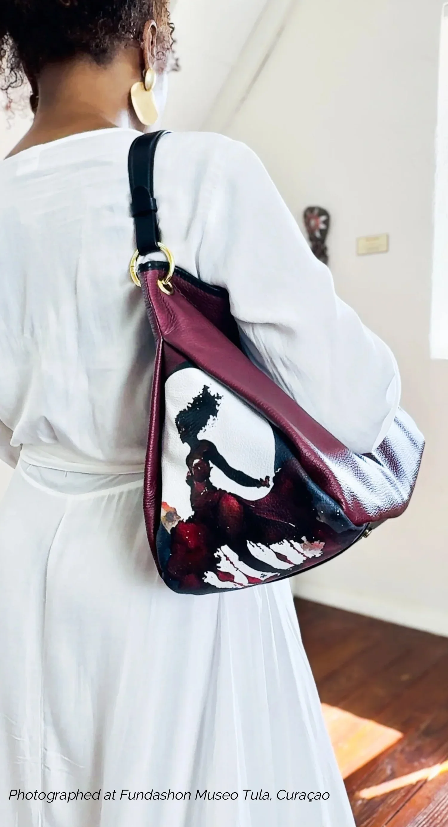A model holding a maroon-colored leather shoulder bag with a unique graphic image of a Moon goddess..
